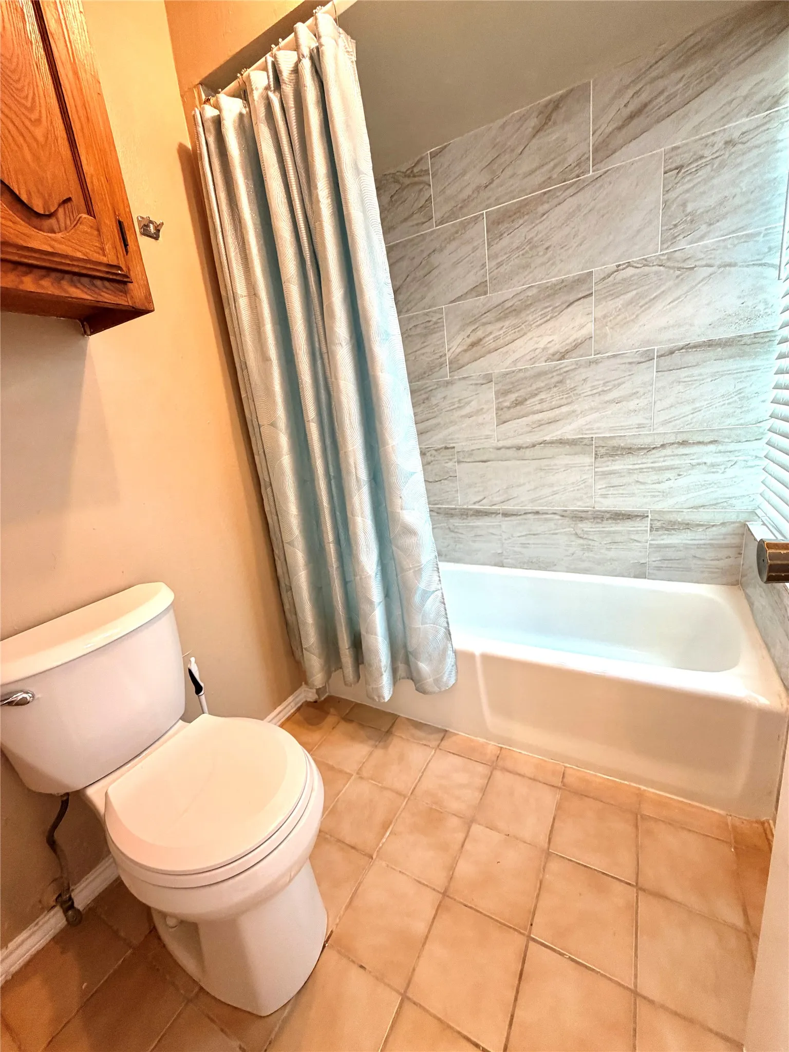 Bathroom featuring a white bathtub with light gray tiled shower surround, a white toilet, and terracotta-toned tile flooring