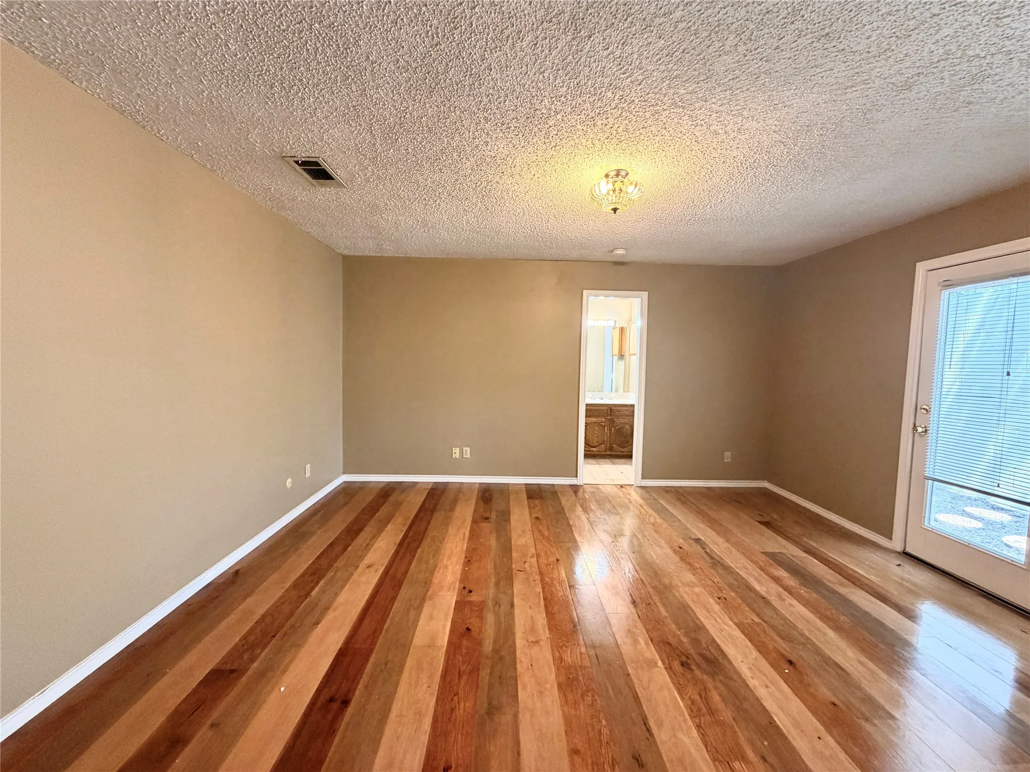 Spacious room featuring multi-tone wood flooring, neutral wall paint, and a textured ceiling