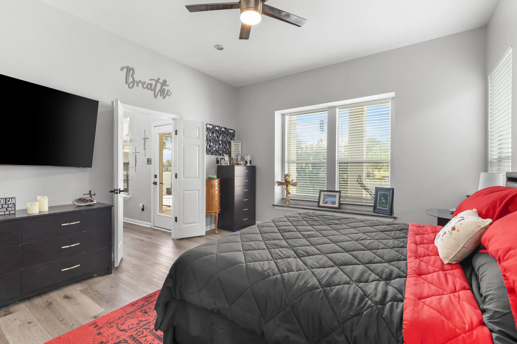 Bright room featuring light gray walls, wood-finish flooring, a ceiling fan with integrated lighting, and a large window with blinds