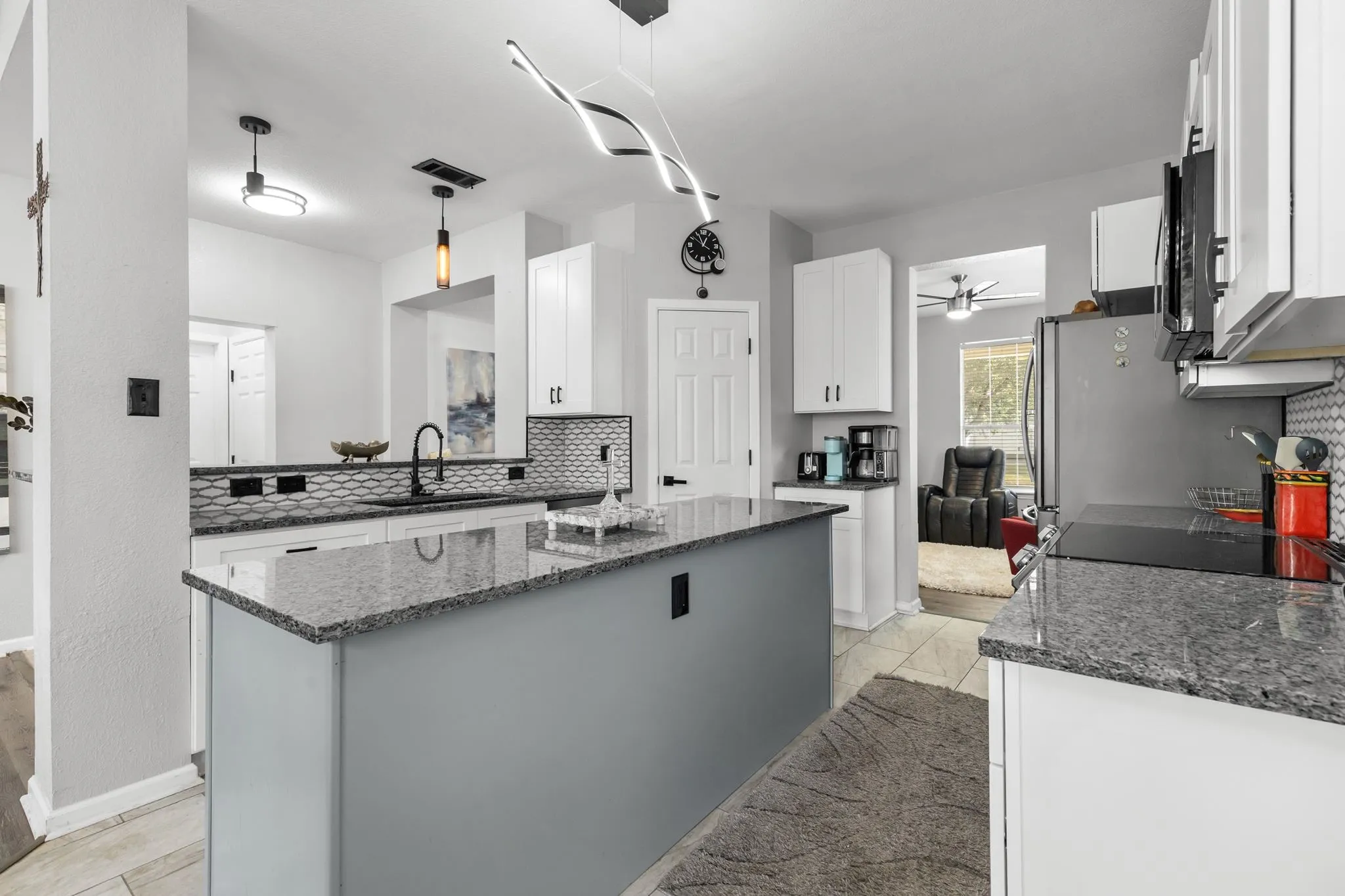 Kitchen featuring a central island with granite countertops, white cabinetry, dark hardware, an undermount sink with a matte black faucet, and patterned backsplash
