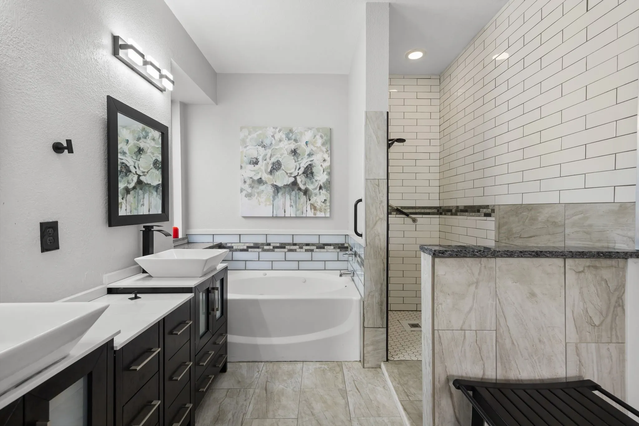 Full bathroom featuring a walk-in shower with subway tile surround, a built-in bathtub with decorative tile accents, and a dual vanity with vessel sinks
