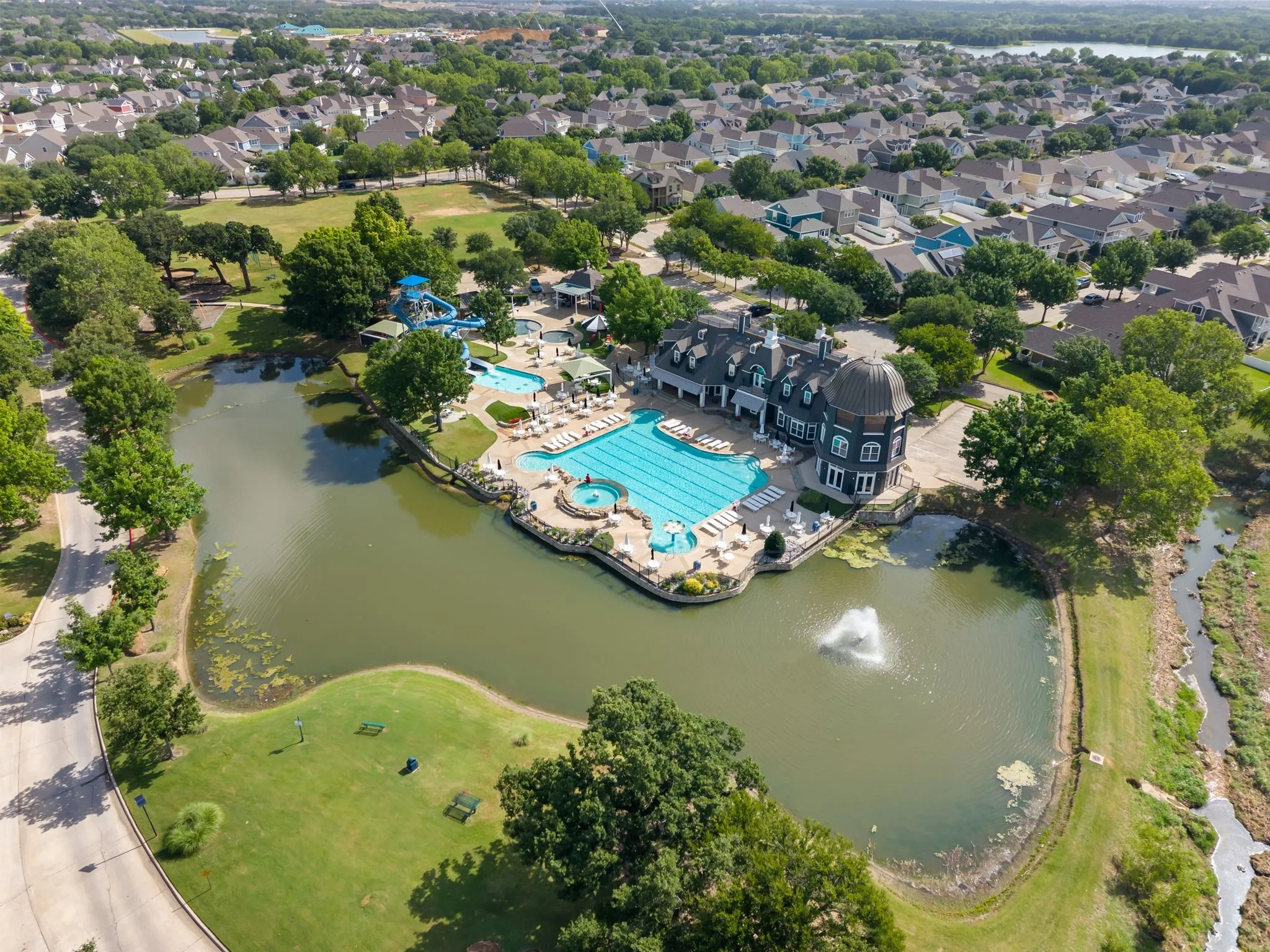Aerial perspective showcasing a large community pool complex with multiple swimming areas, a water slide, and a club house
