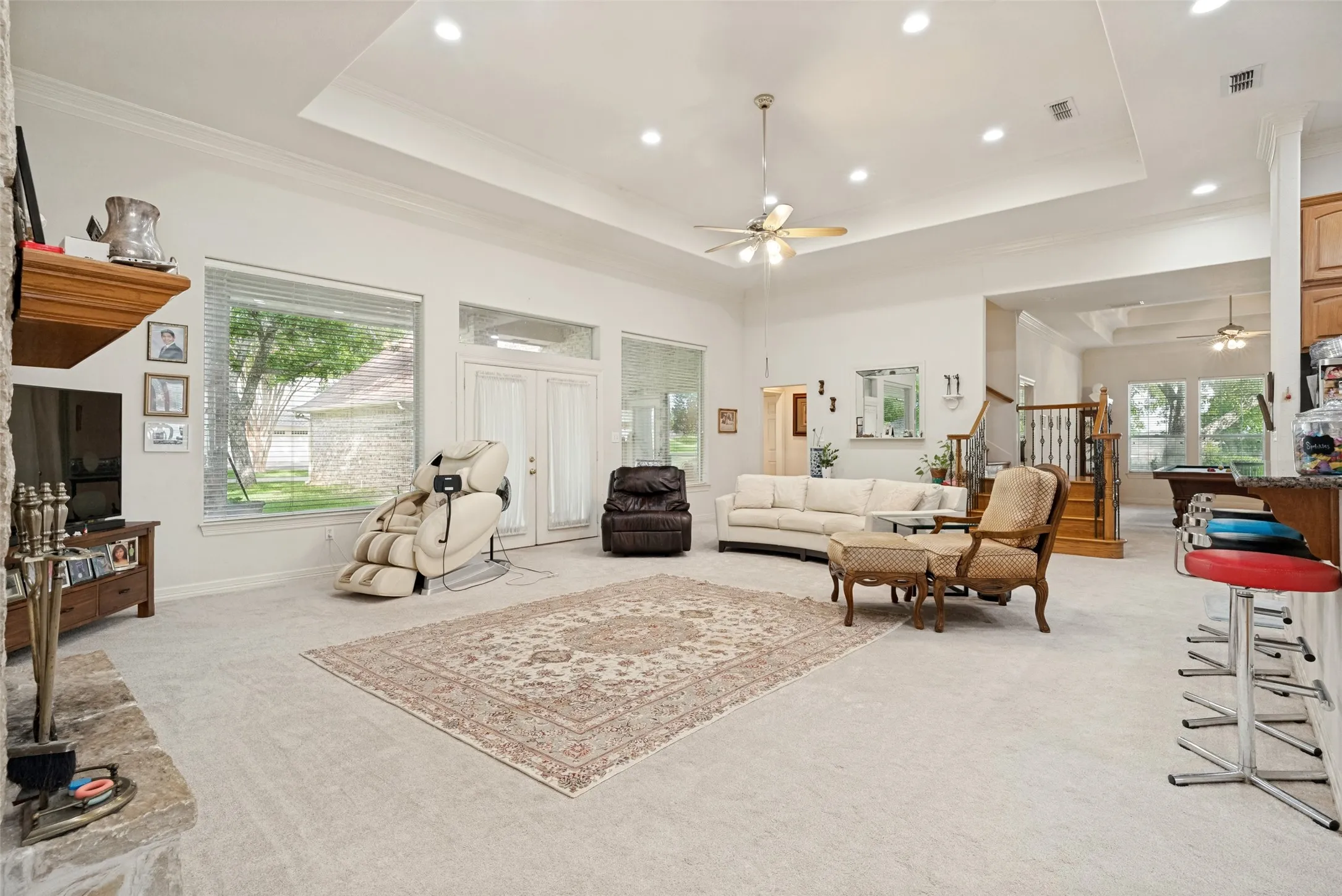 Expansive living area featuring a tray ceiling with recessed lighting, ceiling fan, and light-colored carpeting