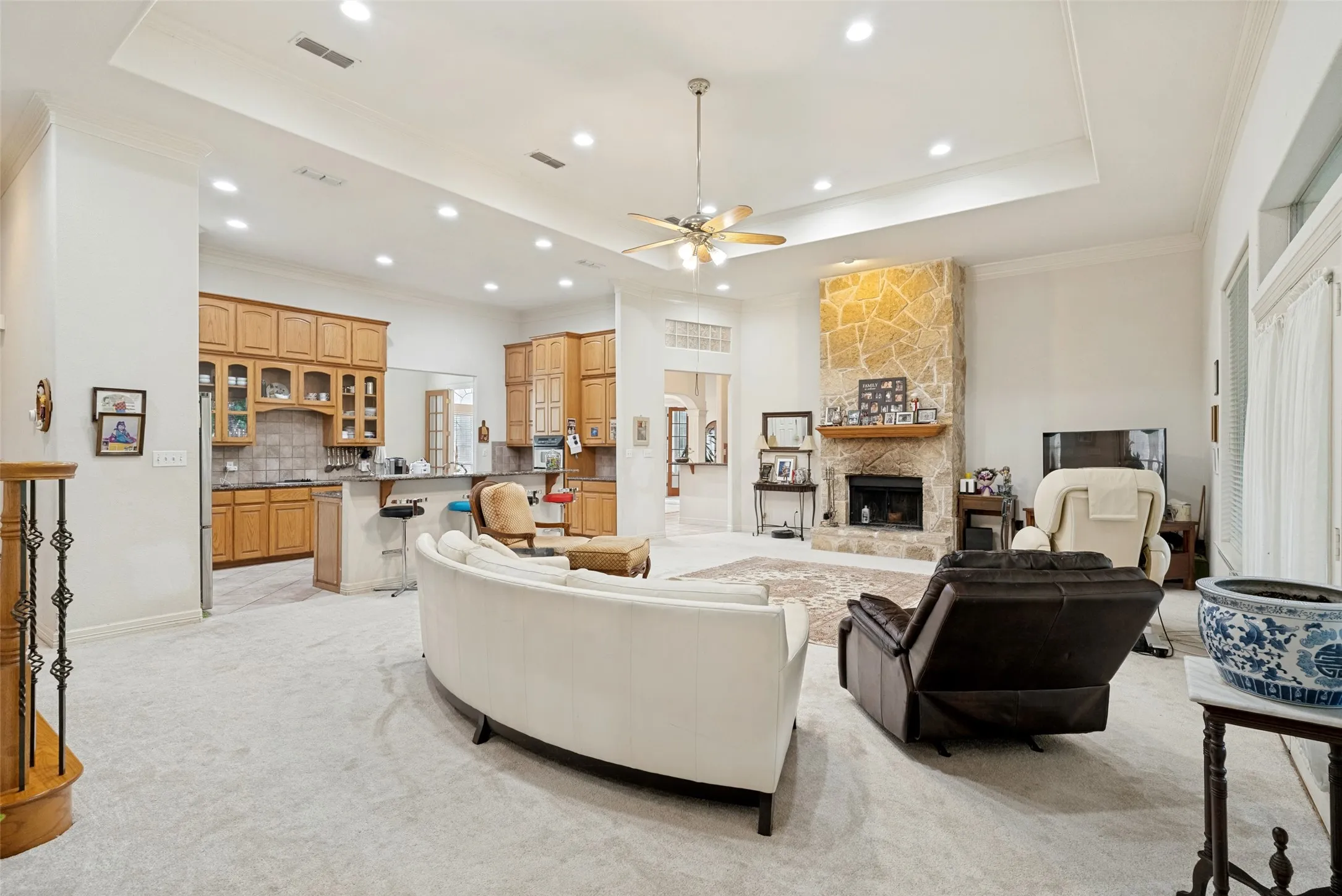 Spacious living area featuring a stone fireplace, recessed lighting, extra large windows, French doors, and a tray ceiling with a ceiling fan