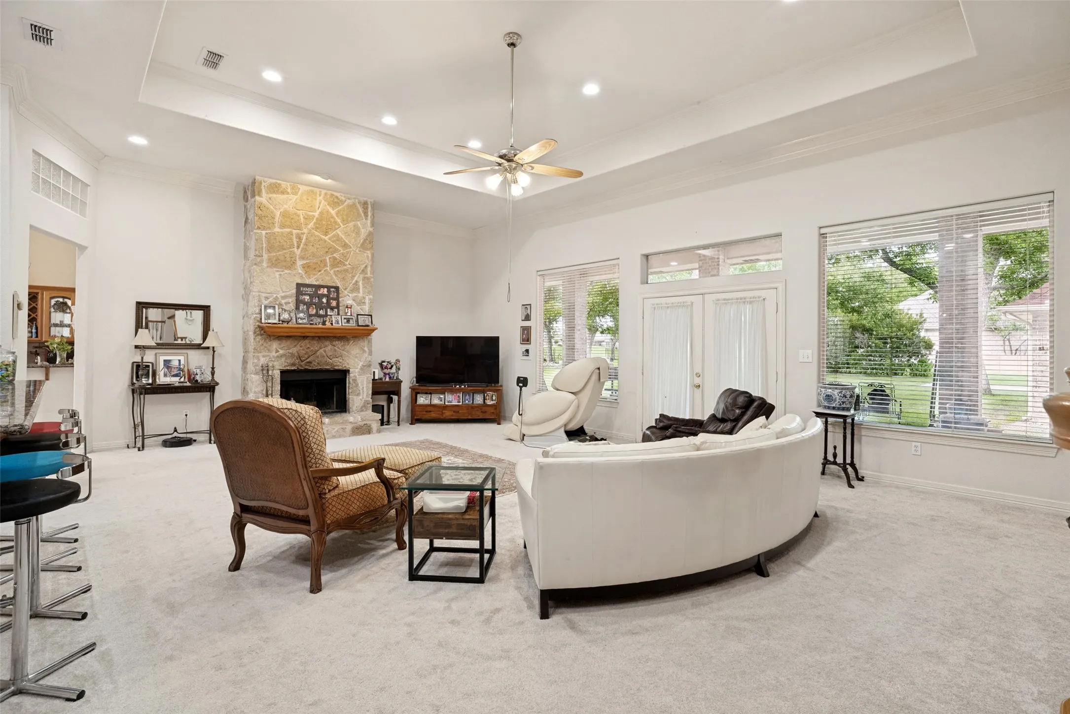 Spacious living area featuring a stone fireplace, recessed lighting, extra large windows, French doors, and a tray ceiling with a ceiling fan