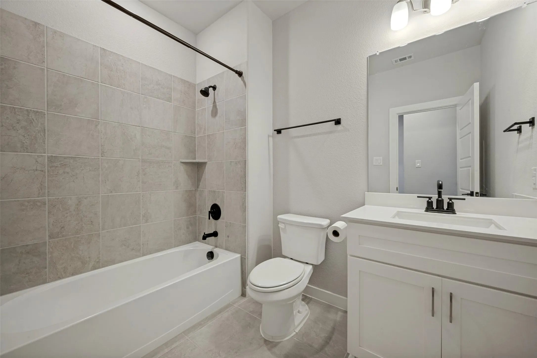 Bathroom featuring a white vanity with integrated sink and white countertop, matte black fixtures, full-width mirror, and a tub-shower combination with light gray tile surround