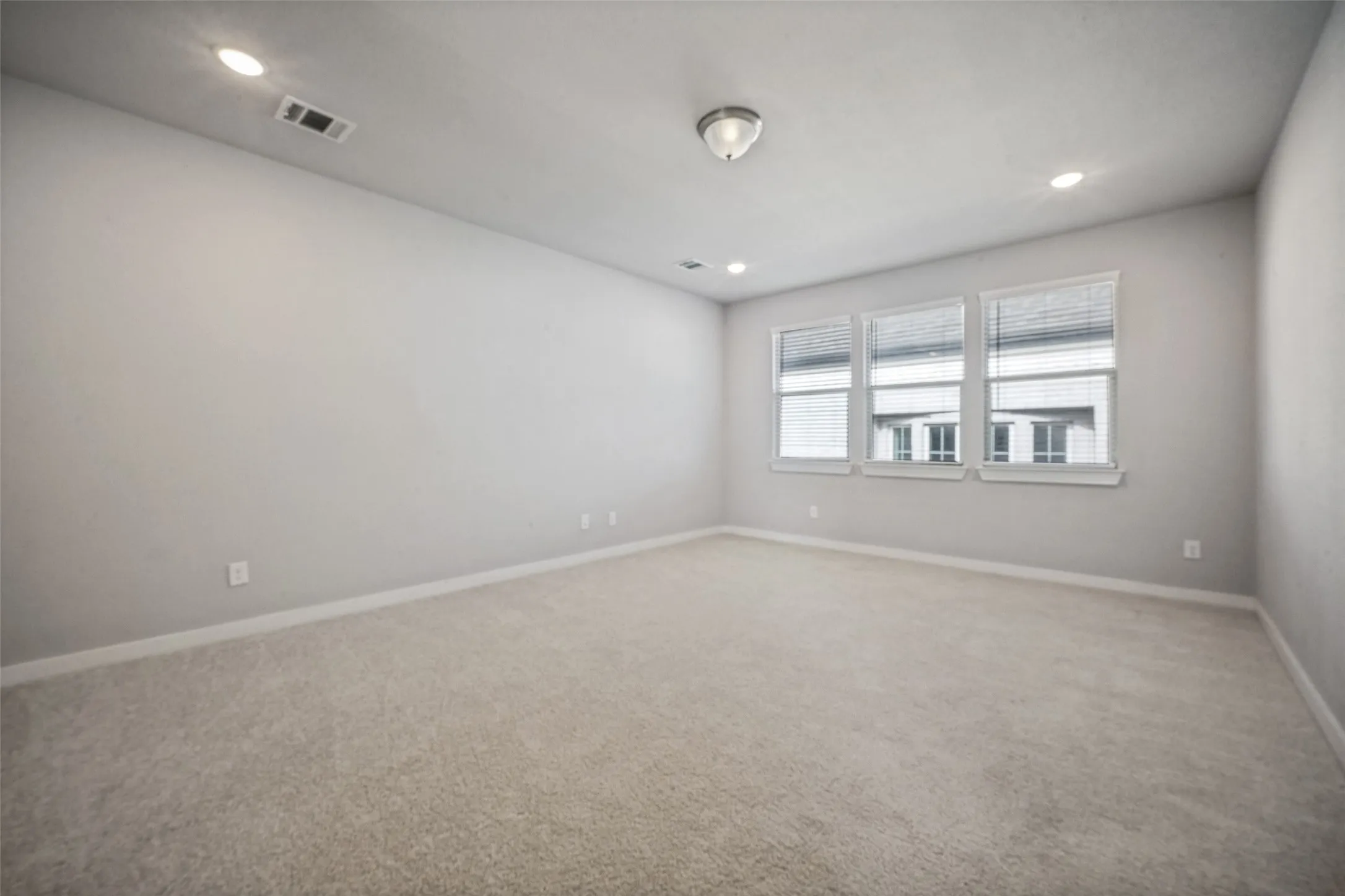 Spacious room featuring neutral carpeting, light-toned walls, and a trio of windows with blinds