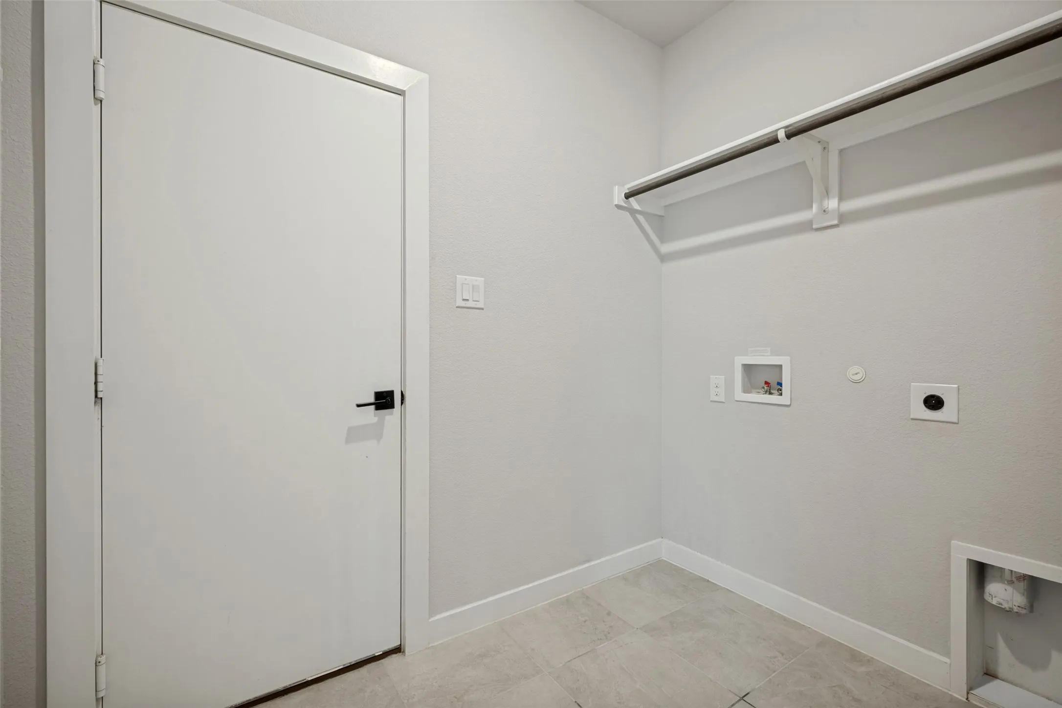 Utility room featuring a built-in hanging rod, wall-mounted shelving, square tile flooring, and white baseboards