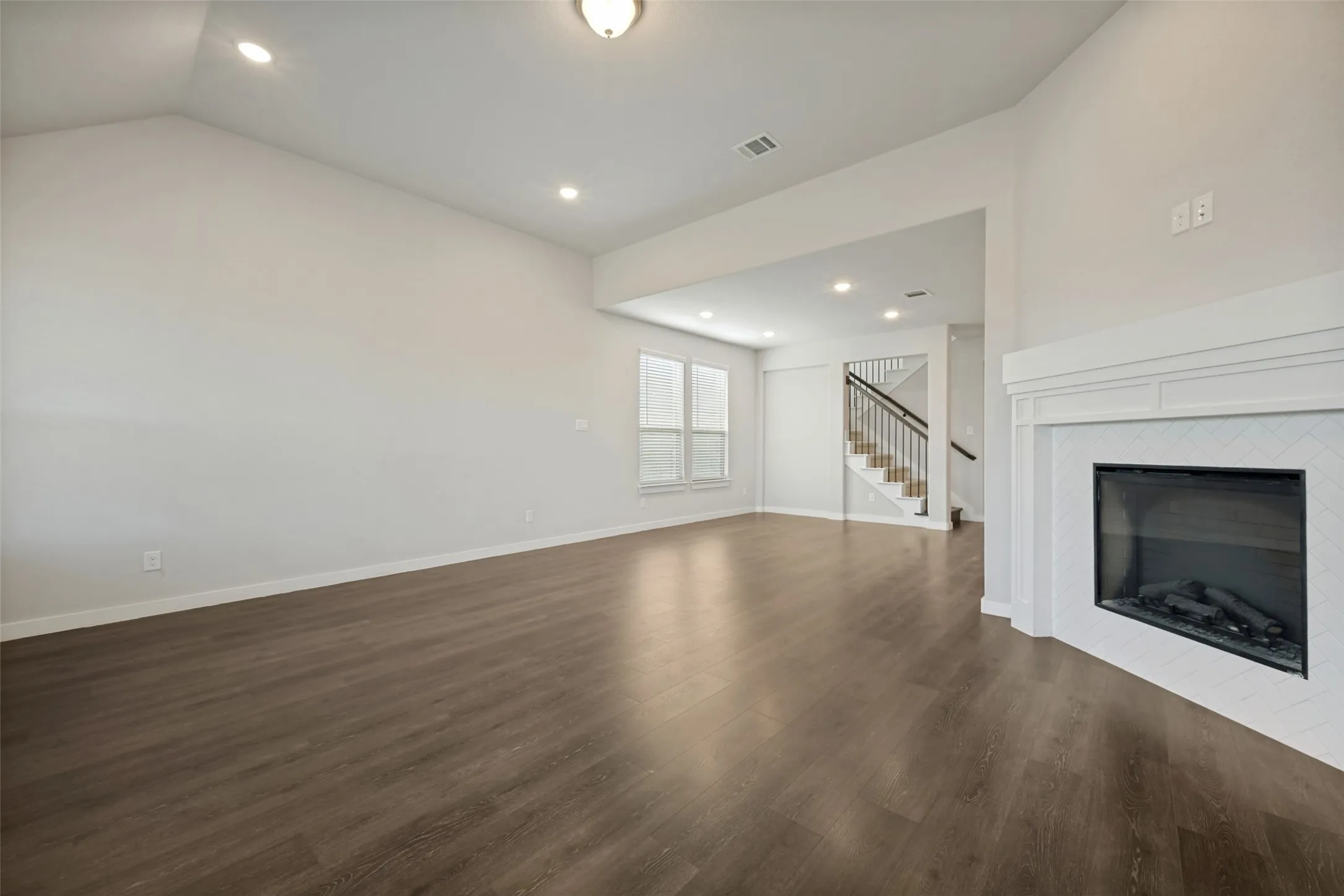Living area featuring wood-finish flooring, a white mantel fireplace with a herringbone tile surround, recessed lighting, and a vaulted ceiling