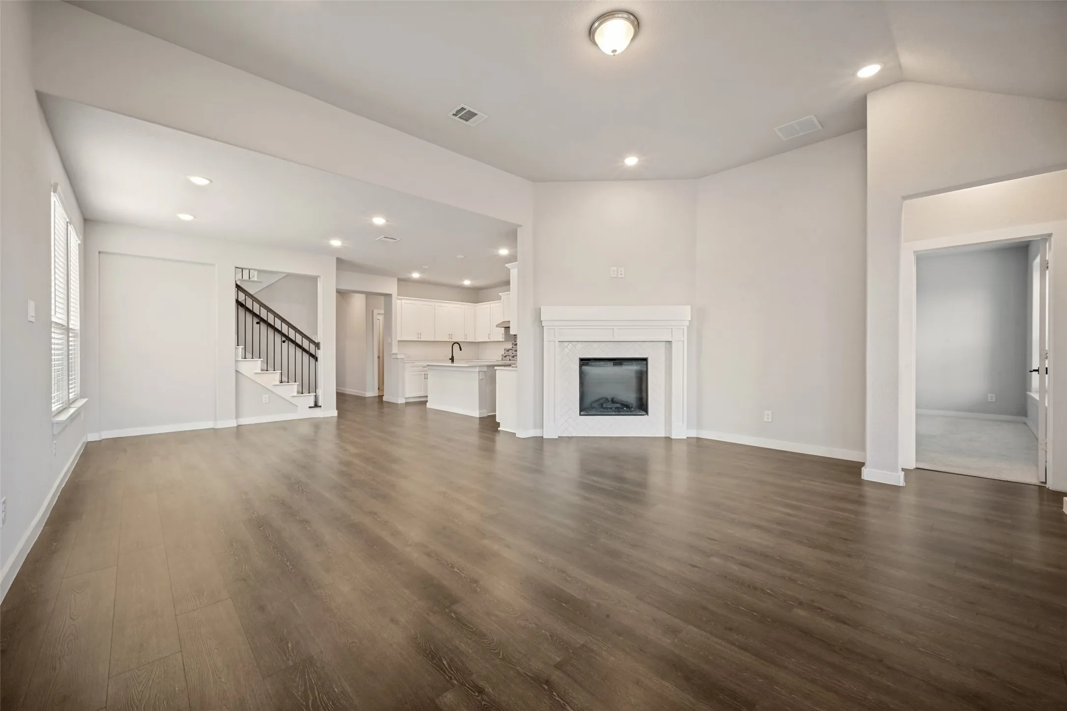Spacious living area featuring wood-finish flooring, a white mantel fireplace, and recessed lighting