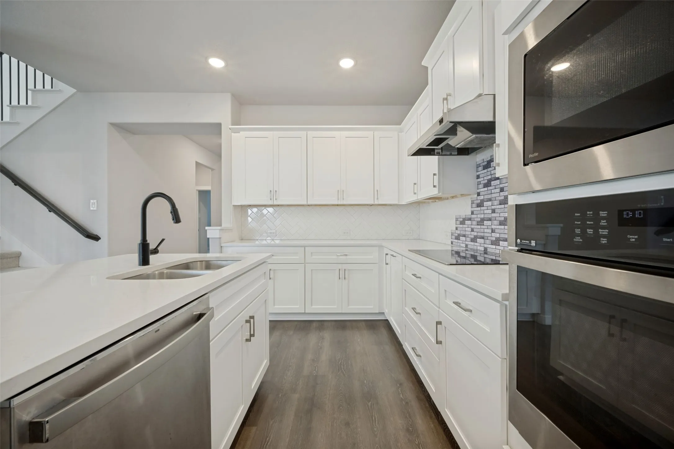 Modern kitchen featuring white cabinetry, light countertops, wood-finish flooring, stainless steel appliances, and a mosaic tile backsplash