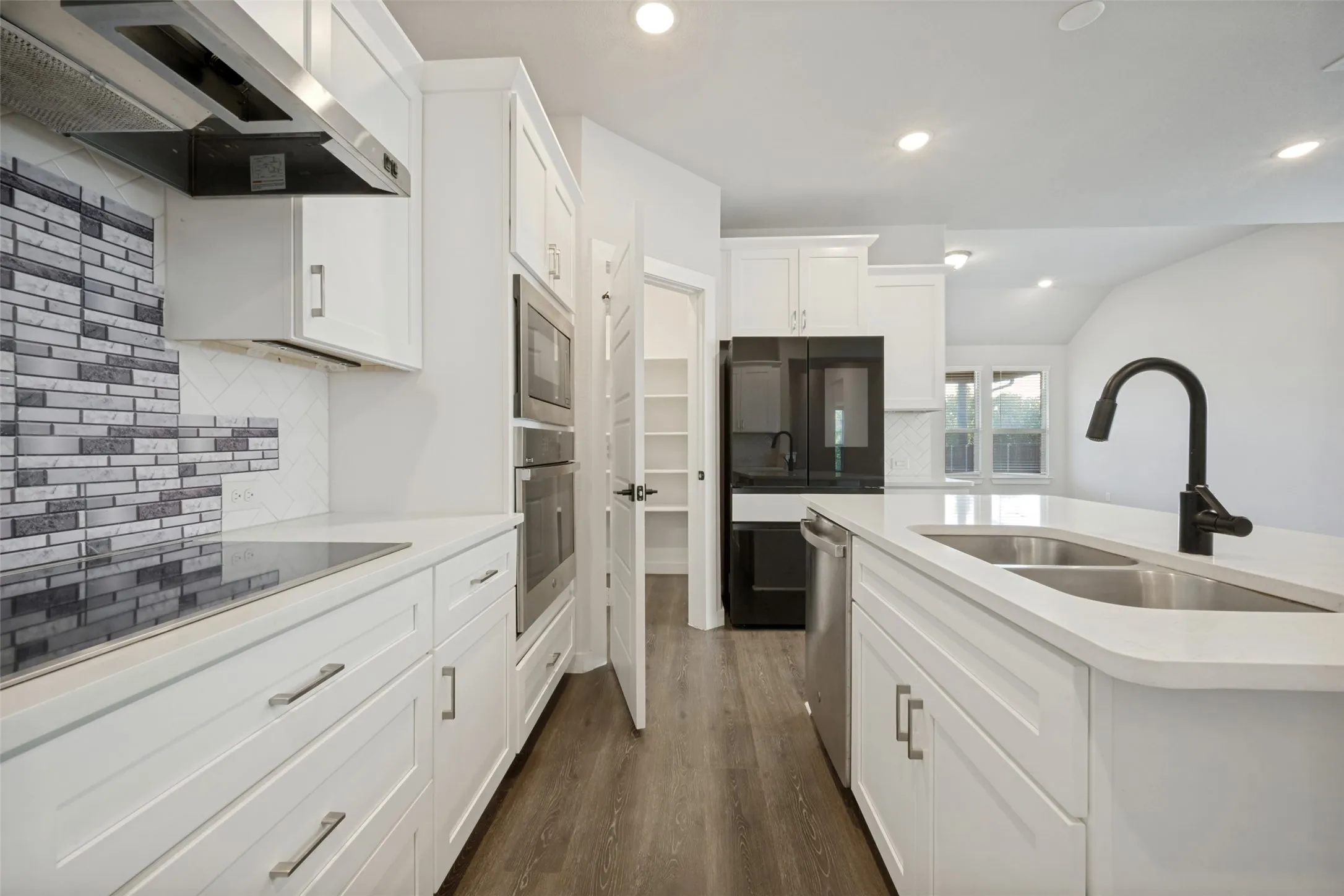 Contemporary kitchen featuring white cabinetry, light countertops, wood-finish flooring, stainless steel appliances, and a mosaic tile backsplash