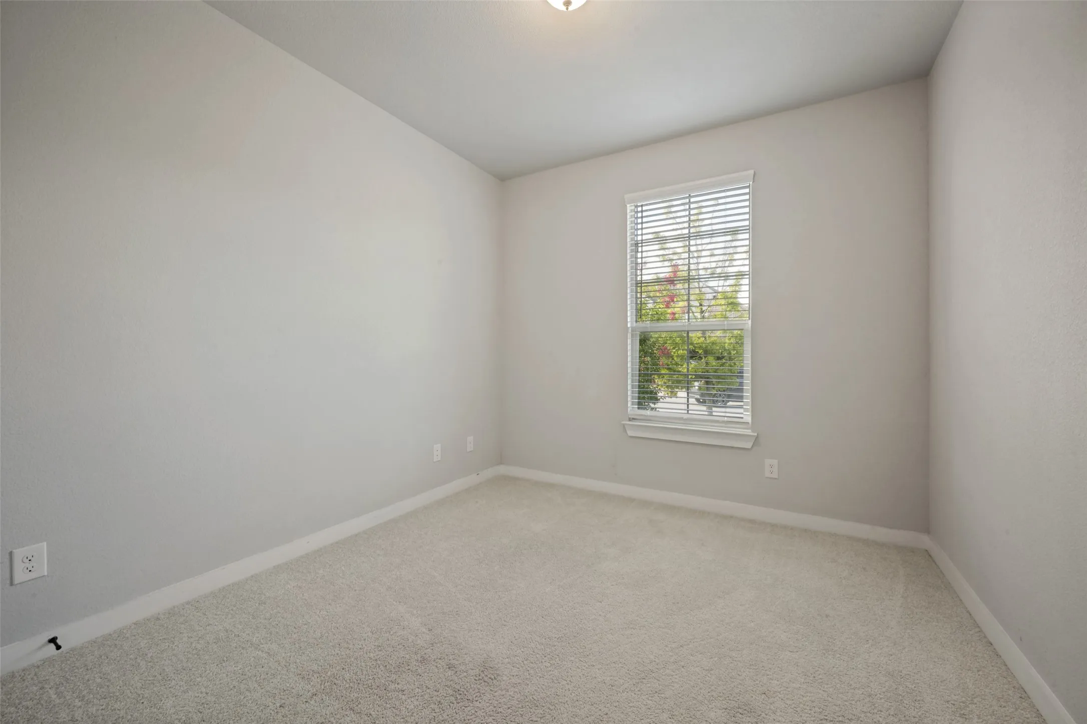 Bedroom featuring soft gray walls, neutral carpeting, a single window with blinds, white baseboards, and a ceiling-mounted light fixture