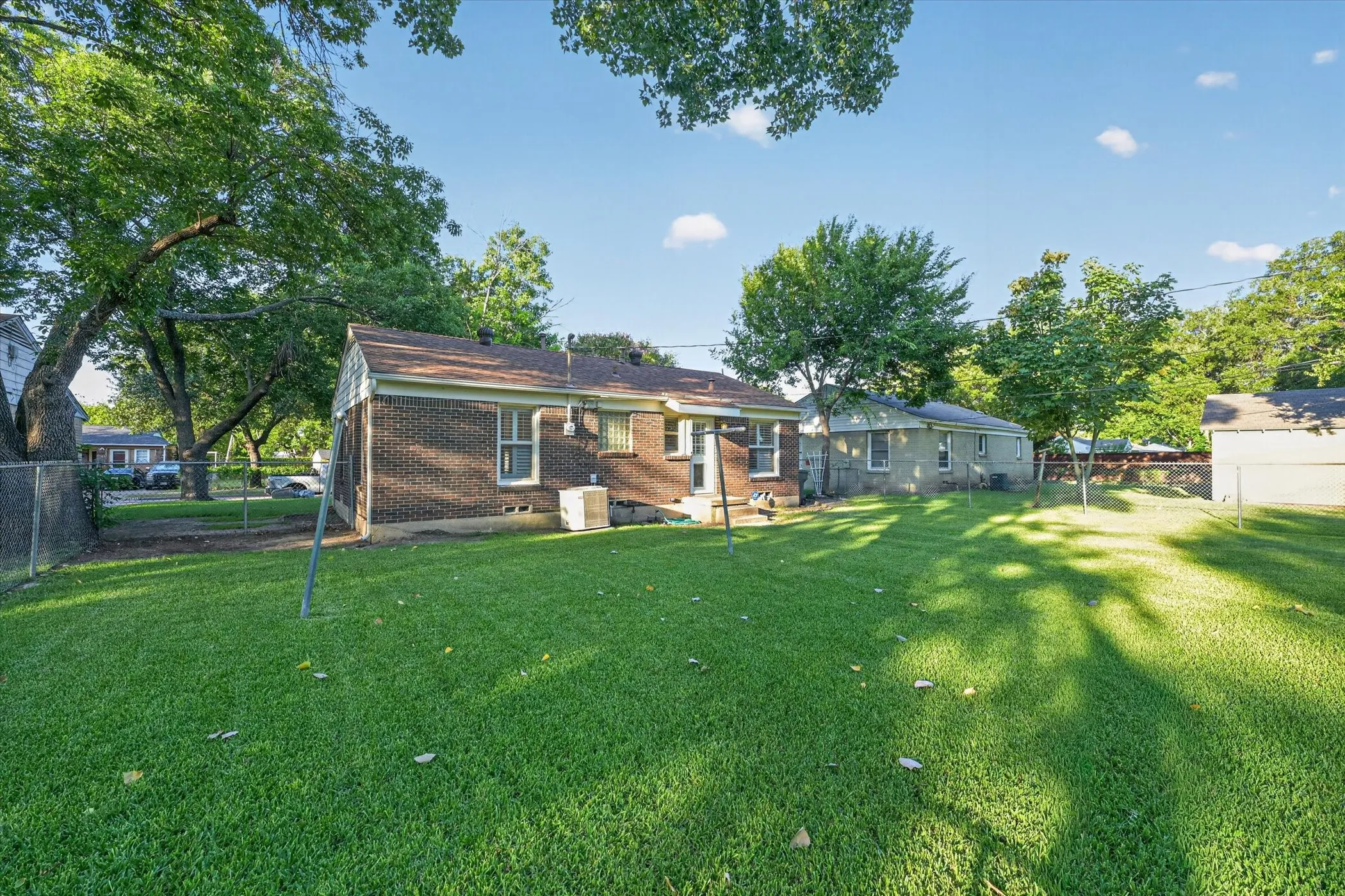 Expansive grassy yard area with partial chain-link fencing, mature trees, and a brick-clad exterior
