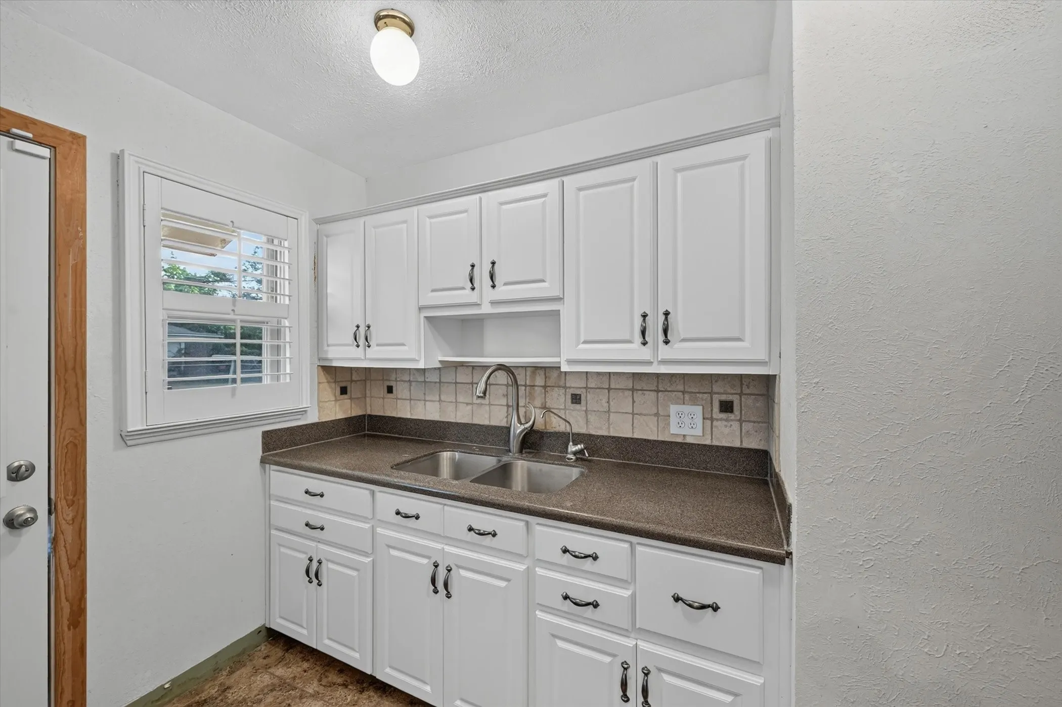 Galley kitchen featuring white cabinetry, a double basin stainless steel sink, and a brown countertop