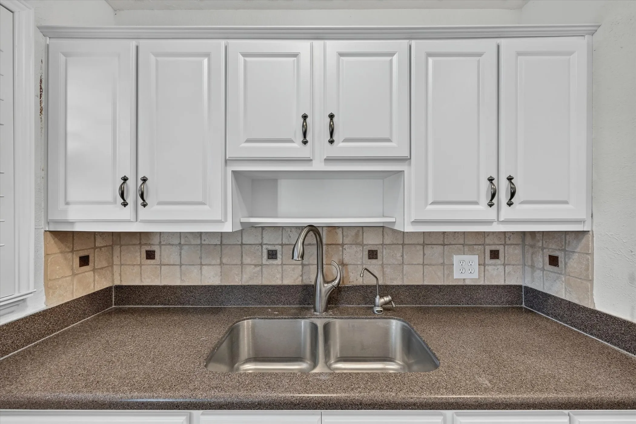 Kitchen sink area featuring white shaker-style cabinetry with dark hardware, a dual-basin stainless steel sink, and a speckled dark countertop