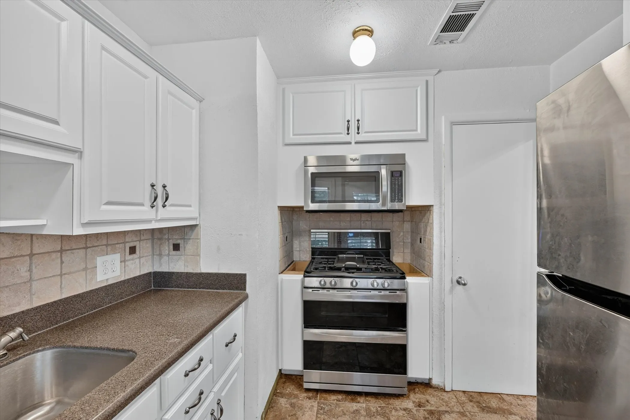 Kitchen featuring white cabinetry with dark hardware, a stainless steel gas range, a stainless steel microwave, a stainless steel refrigerator, and a stainless steel sink with a single-handle faucet