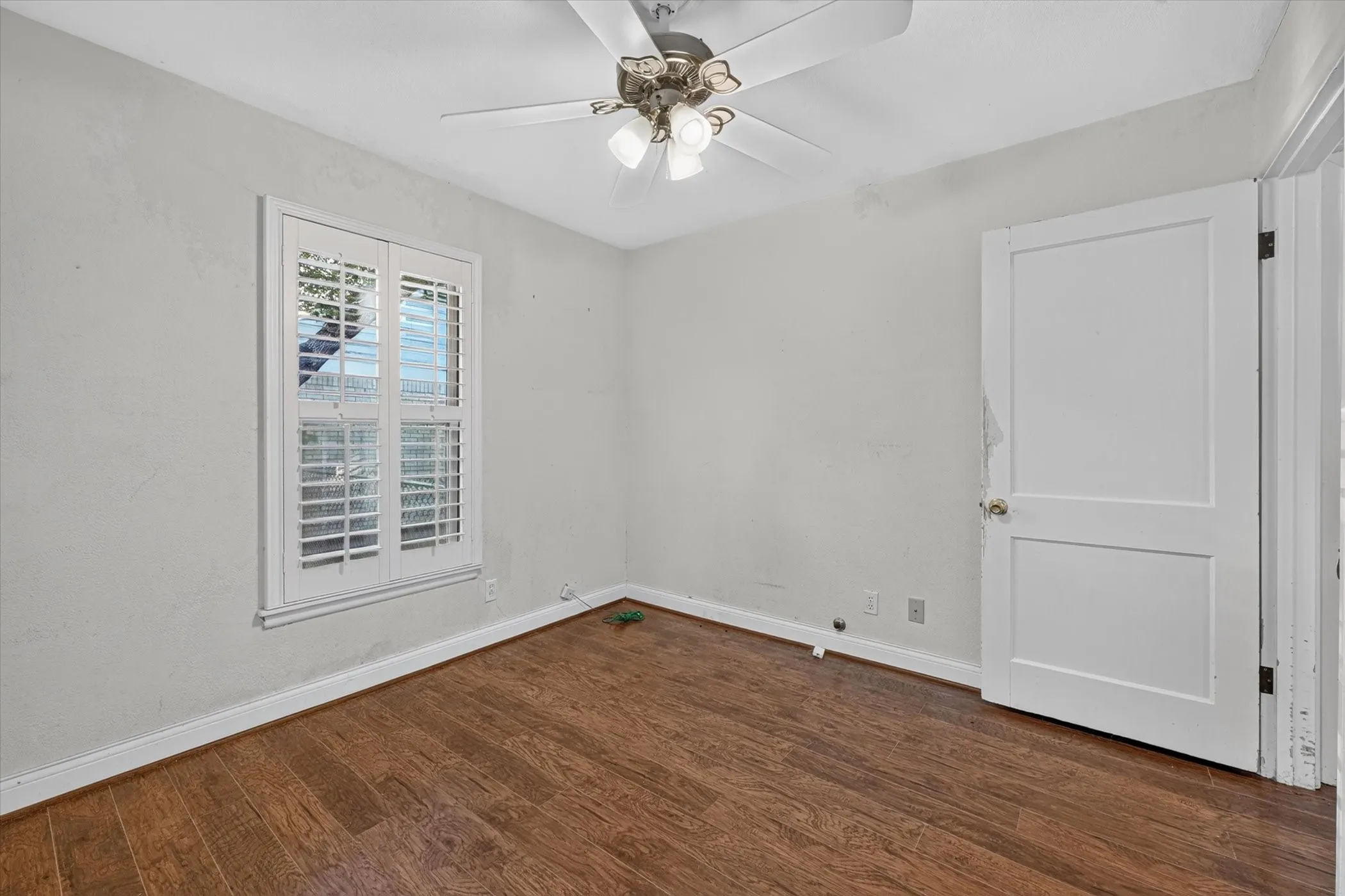 Room featuring wood-finish flooring, a ceiling fan with integrated lighting, and a window with white plantation shutters