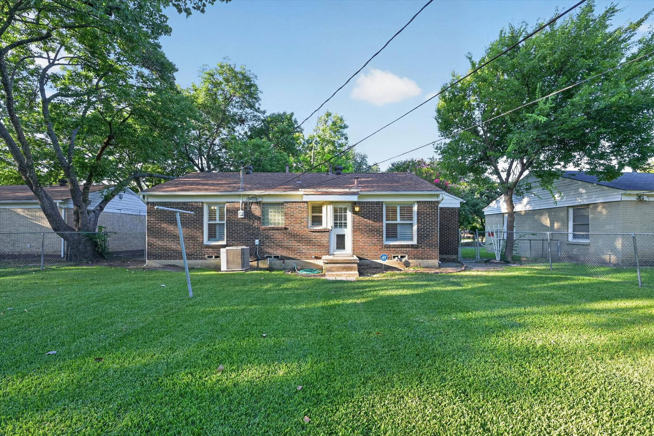 Spacious backyard featuring a manicured lawn, established shade trees, and a chain-link fence