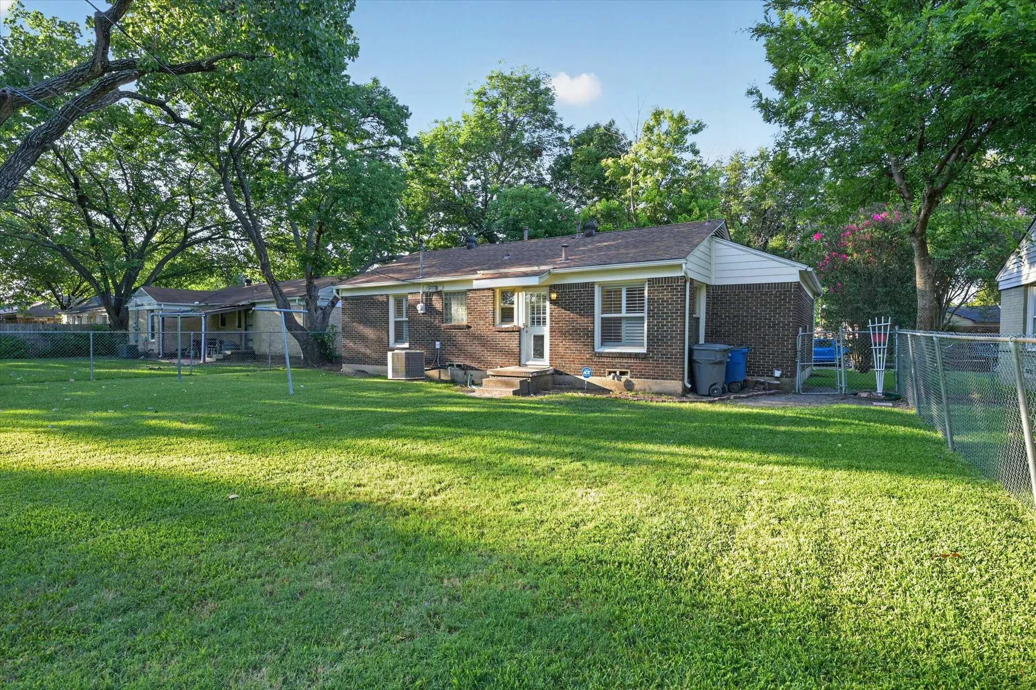 Expansive rear lawn featuring mature trees and a chain-link perimeter fence