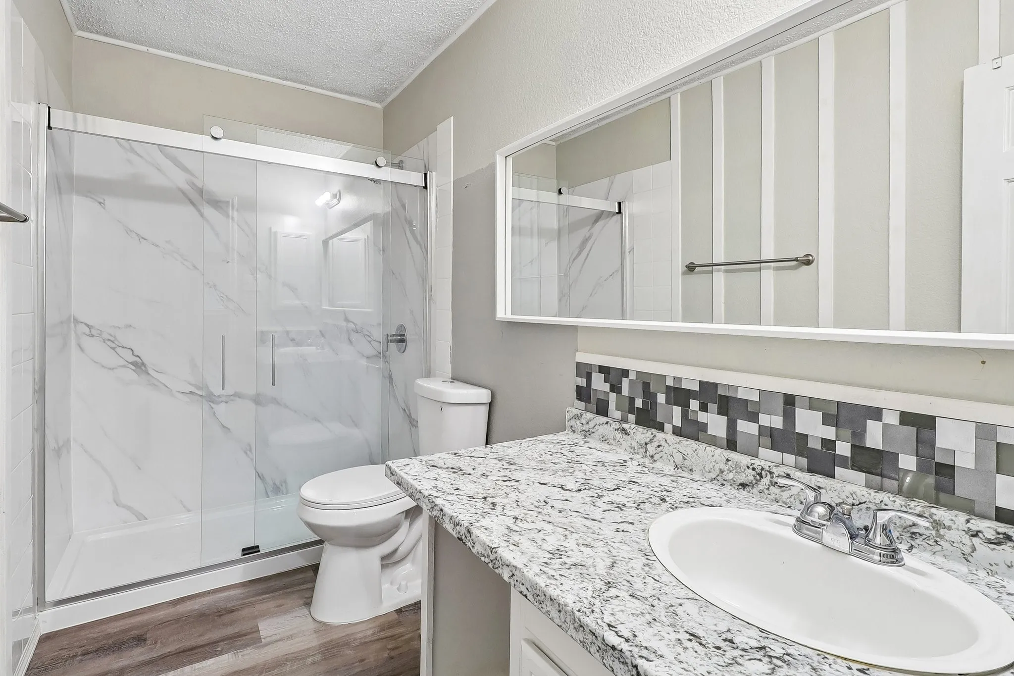 Bathroom featuring a walk-in shower with clear glass doors and marble-look wall panels