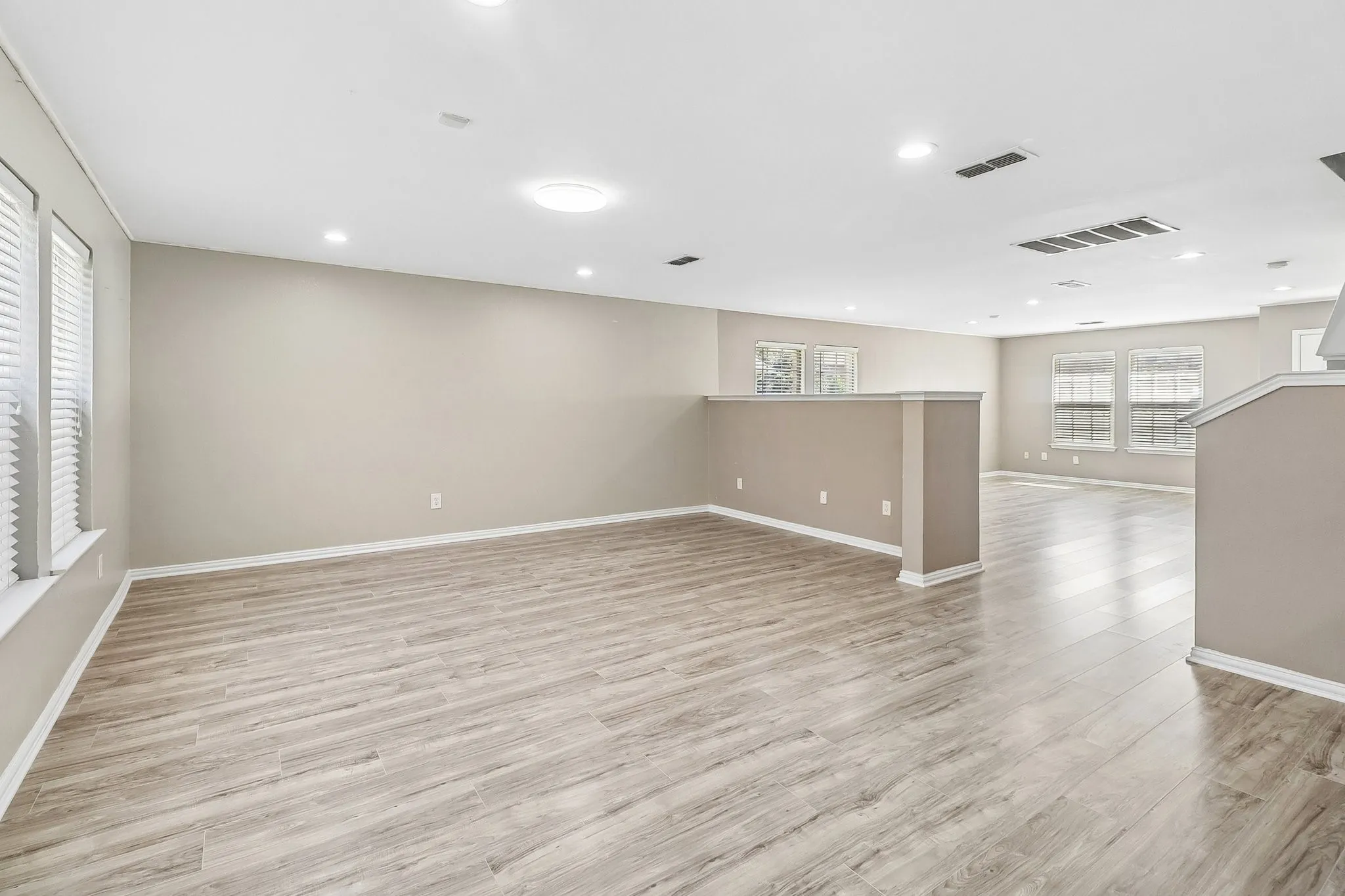 Expansive open-concept room featuring light wood-finish flooring, recessed lighting, multiple windows with blinds, and neutral wall paint