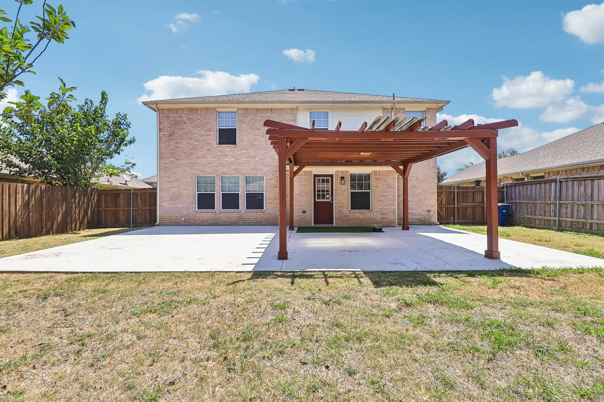 Expansive concrete patio featuring a wood pergola structure, enclosed by privacy fencing