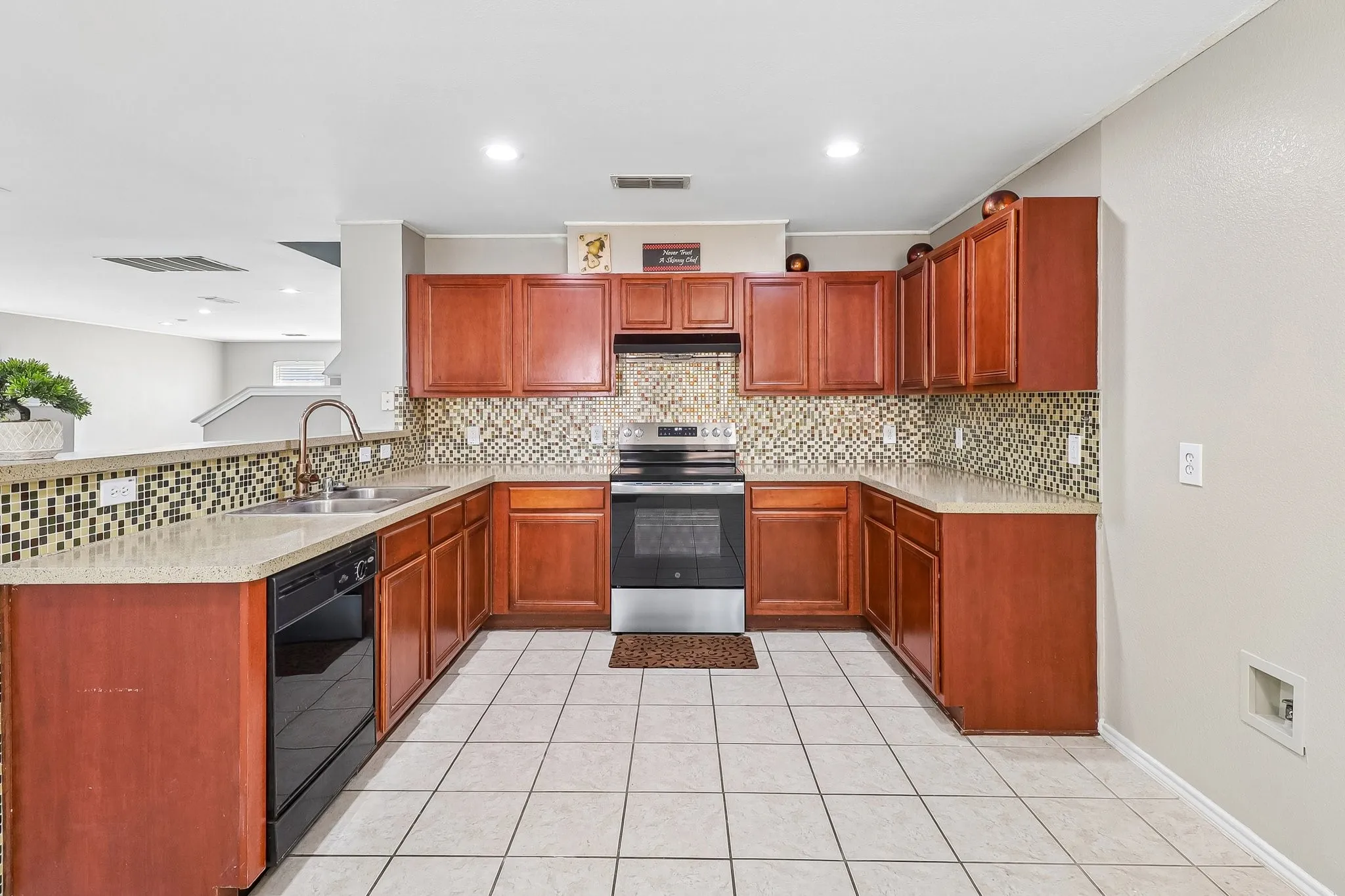 U-shaped kitchen featuring wood cabinetry, stone-finish countertops, and a mosaic tile backsplash