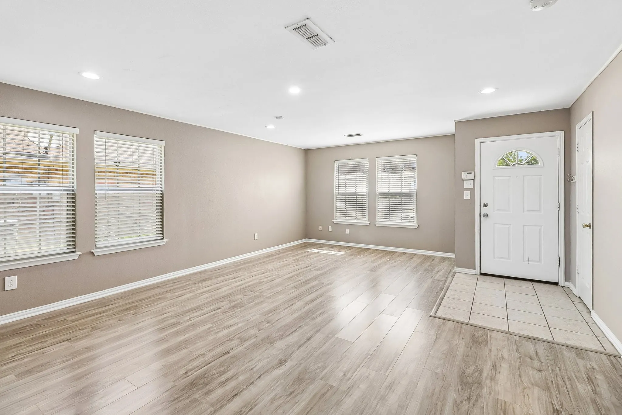 Spacious room featuring wood-finish flooring, neutral-toned walls, recessed lighting, and multiple windows with blinds