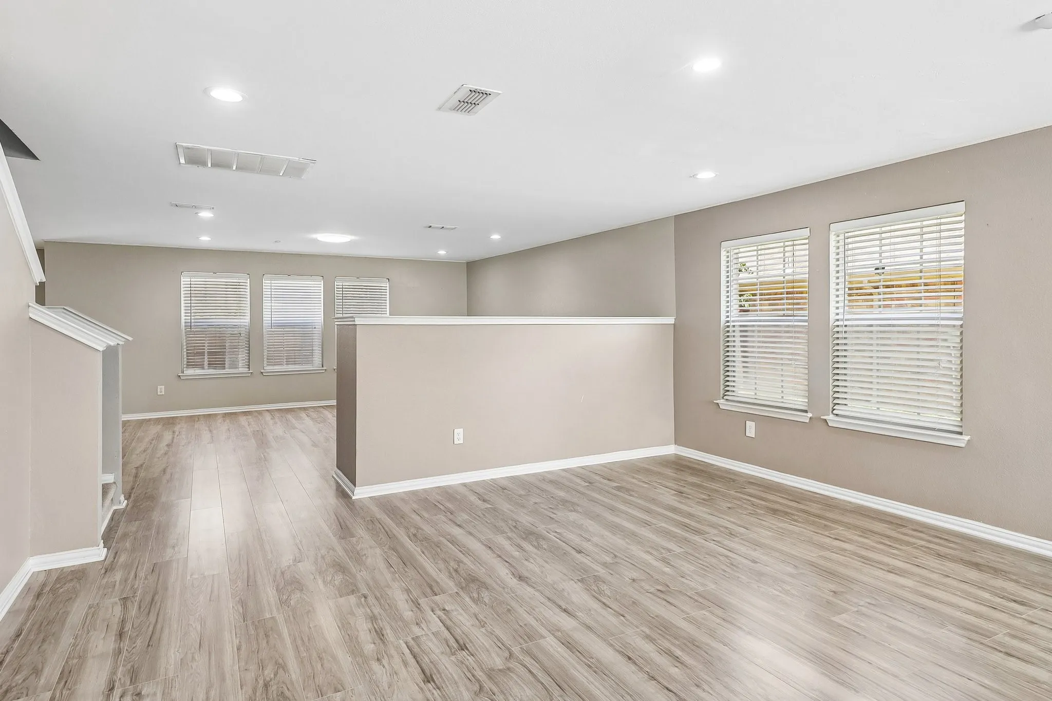 Spacious room featuring wood-finish flooring, multiple windows, recessed lighting, and neutral wall tones