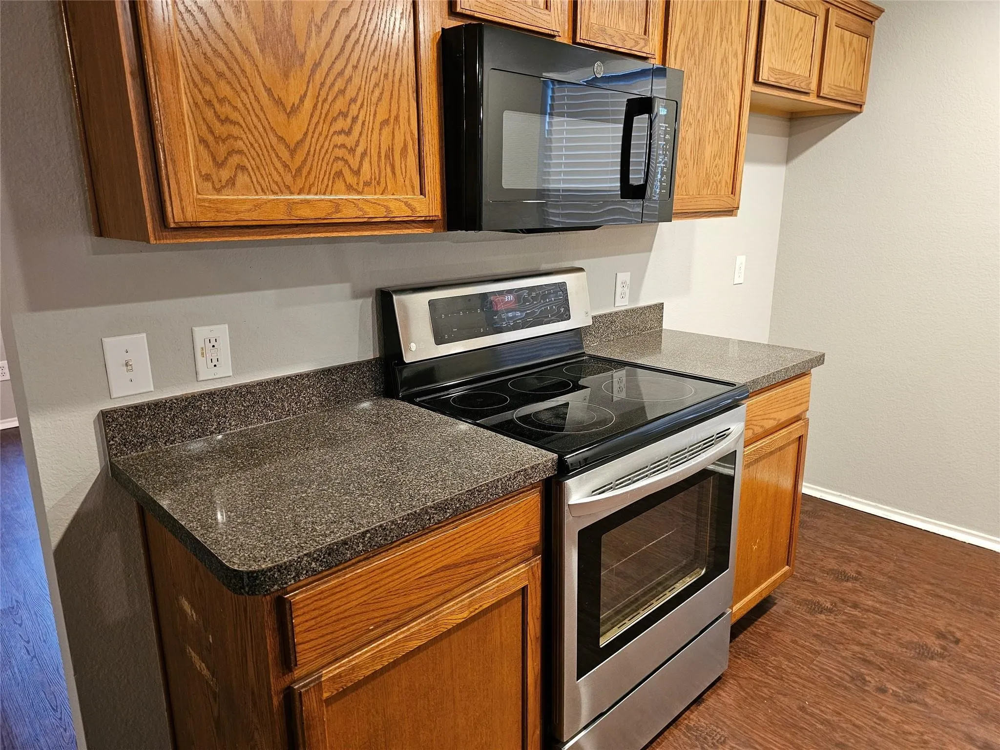 Kitchen featuring stainless steel electric range oven, dark countertops, brown cabinets, and black microwave