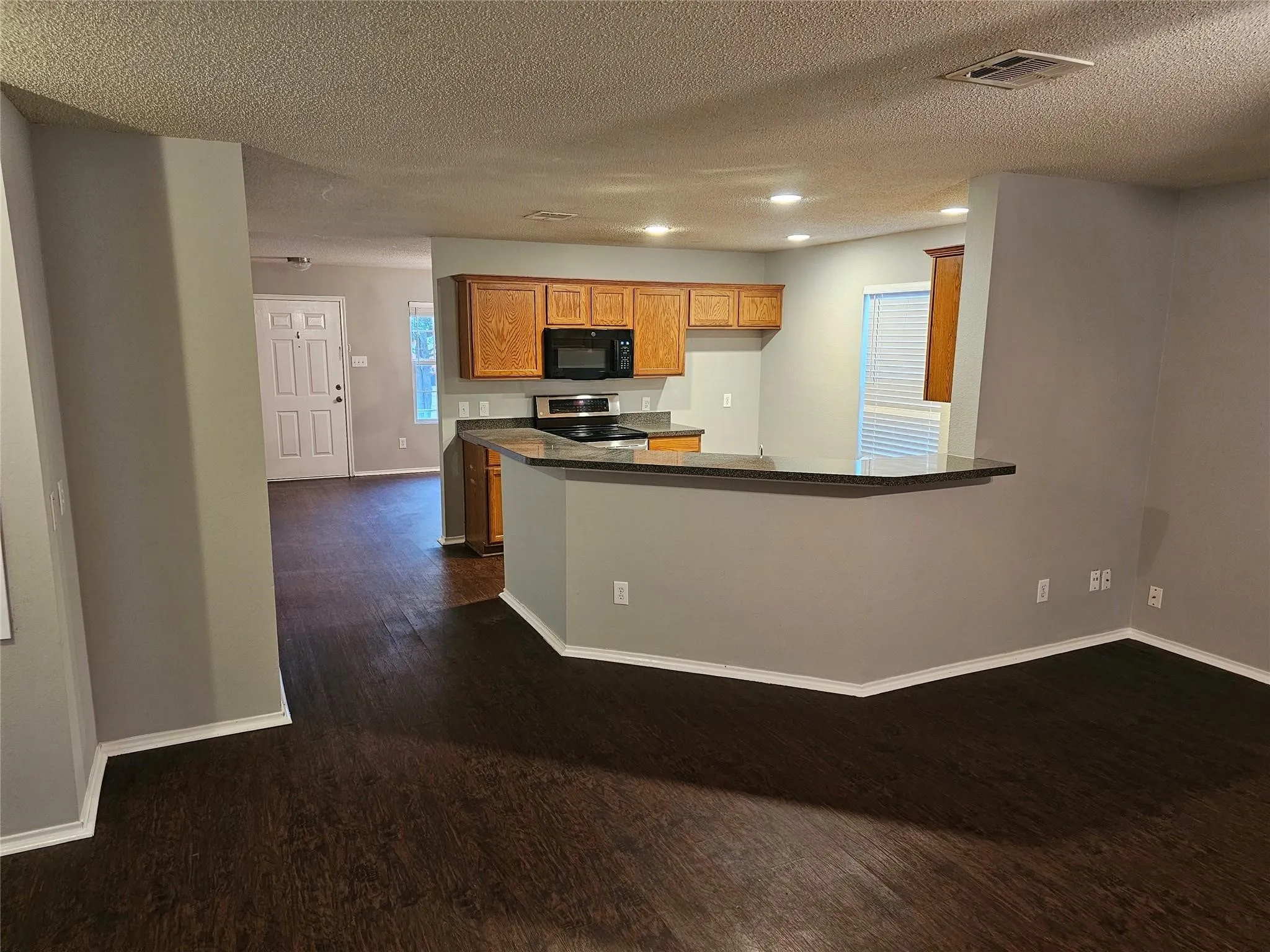 Kitchen with dark wood-type flooring, brown cabinetry, a peninsula, a textured ceiling, and black microwave