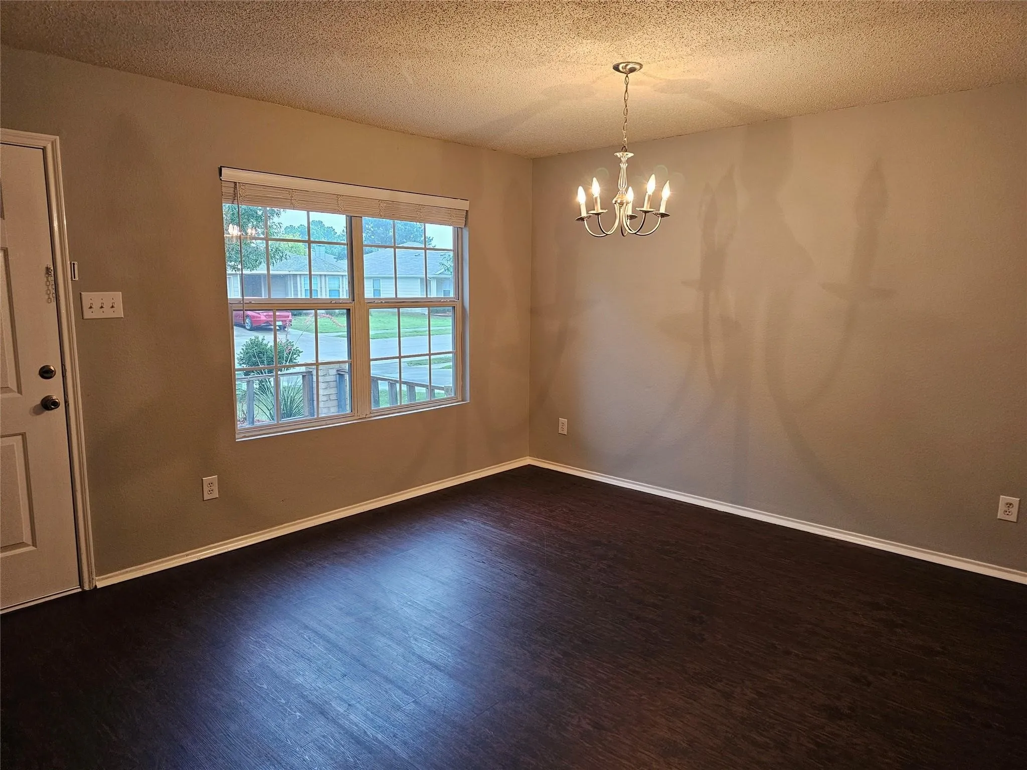 Unfurnished dining area featuring dark wood-type flooring, a textured ceiling, and a chandelier