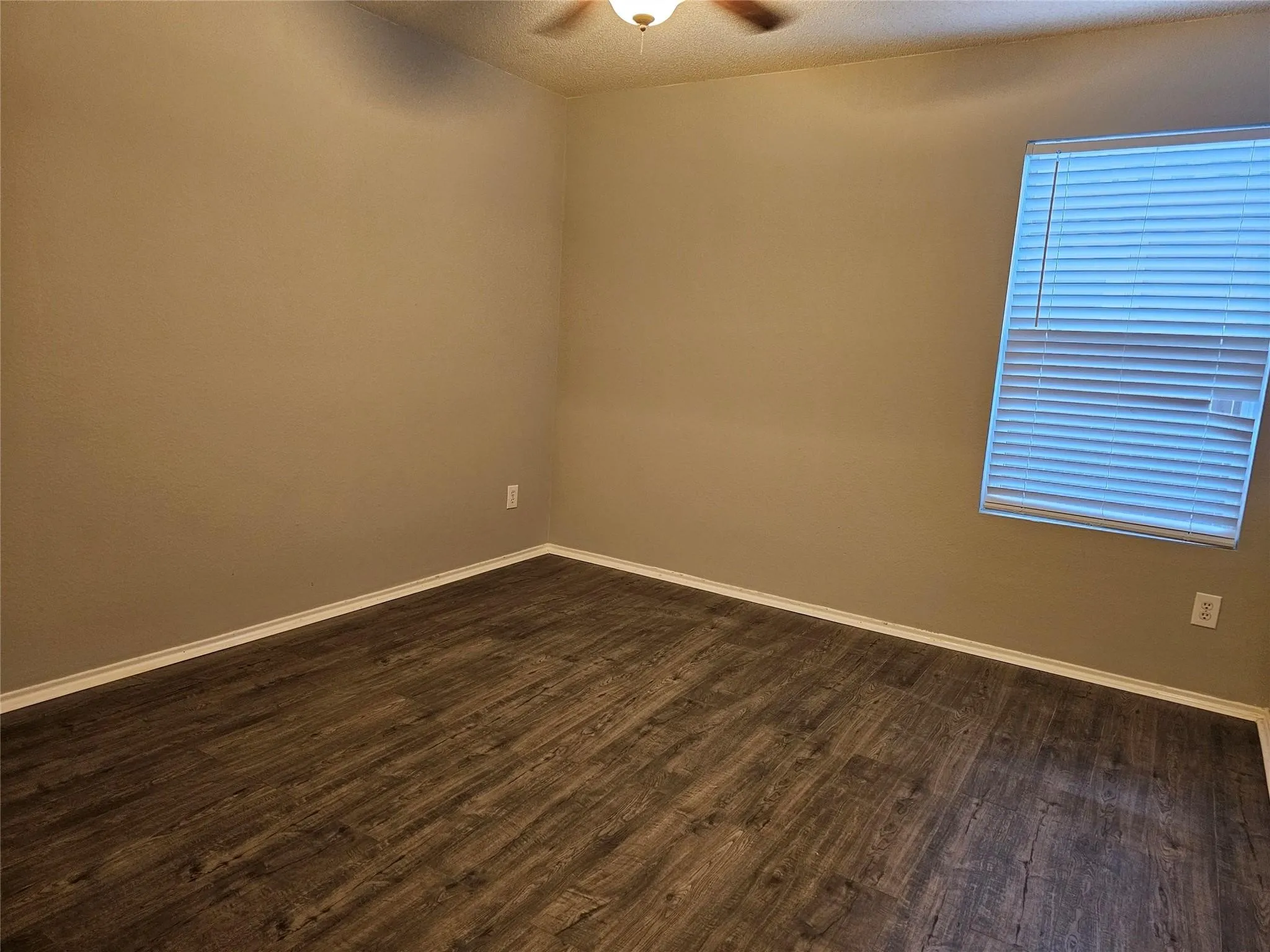 Empty room featuring a textured ceiling, dark wood-type flooring, and ceiling fan