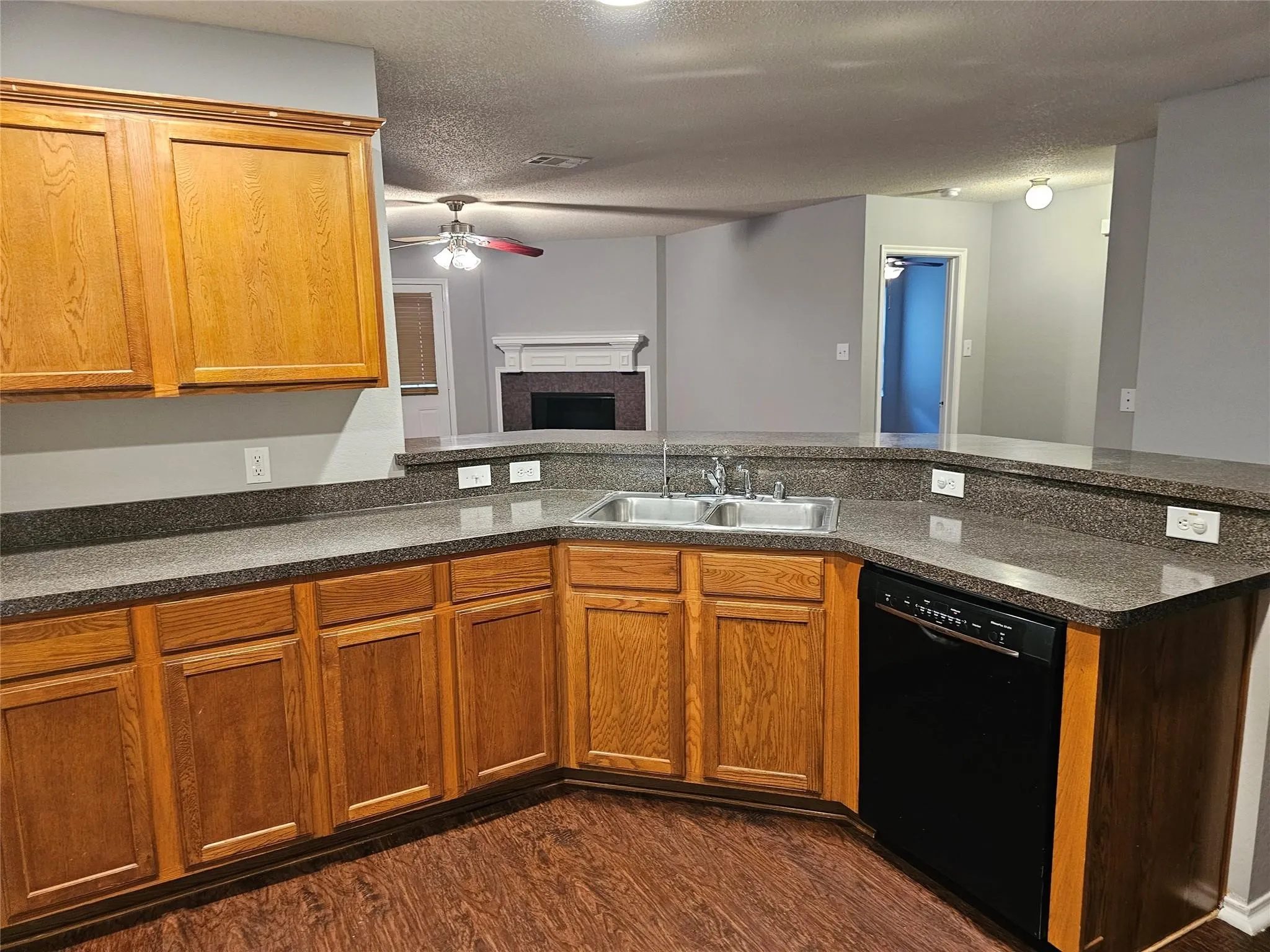 Kitchen featuring black dishwasher, ceiling fan, brown cabinetry, and a textured ceiling