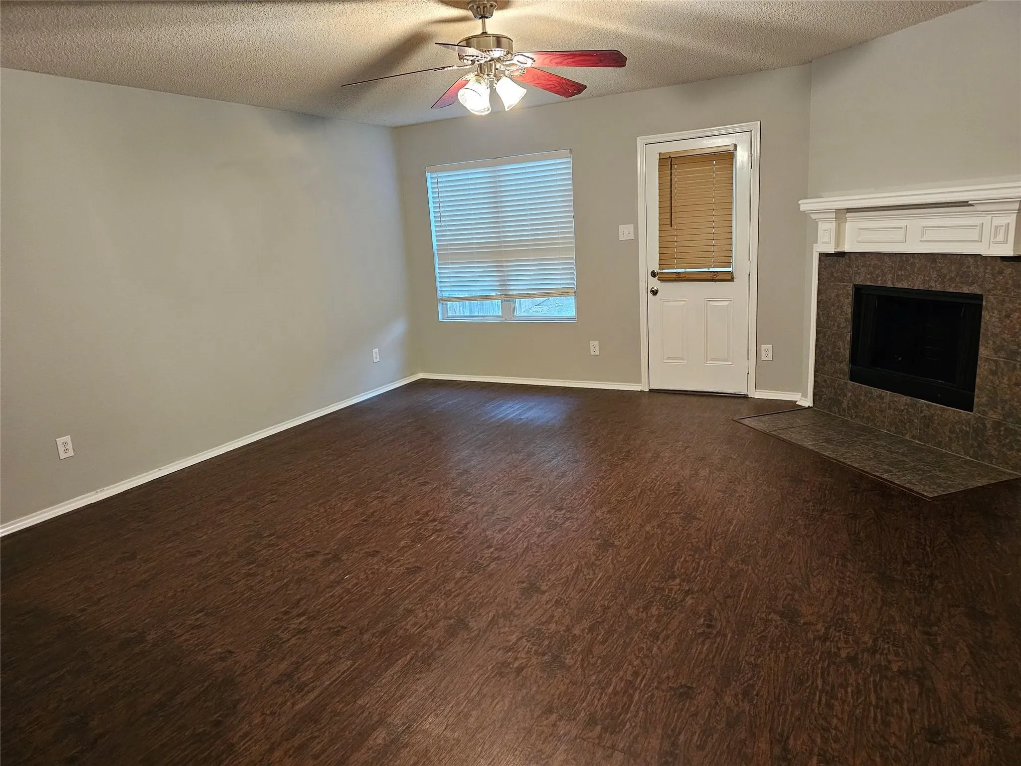 Unfurnished living room with a textured ceiling, a tiled fireplace, dark wood-type flooring, and a ceiling fan