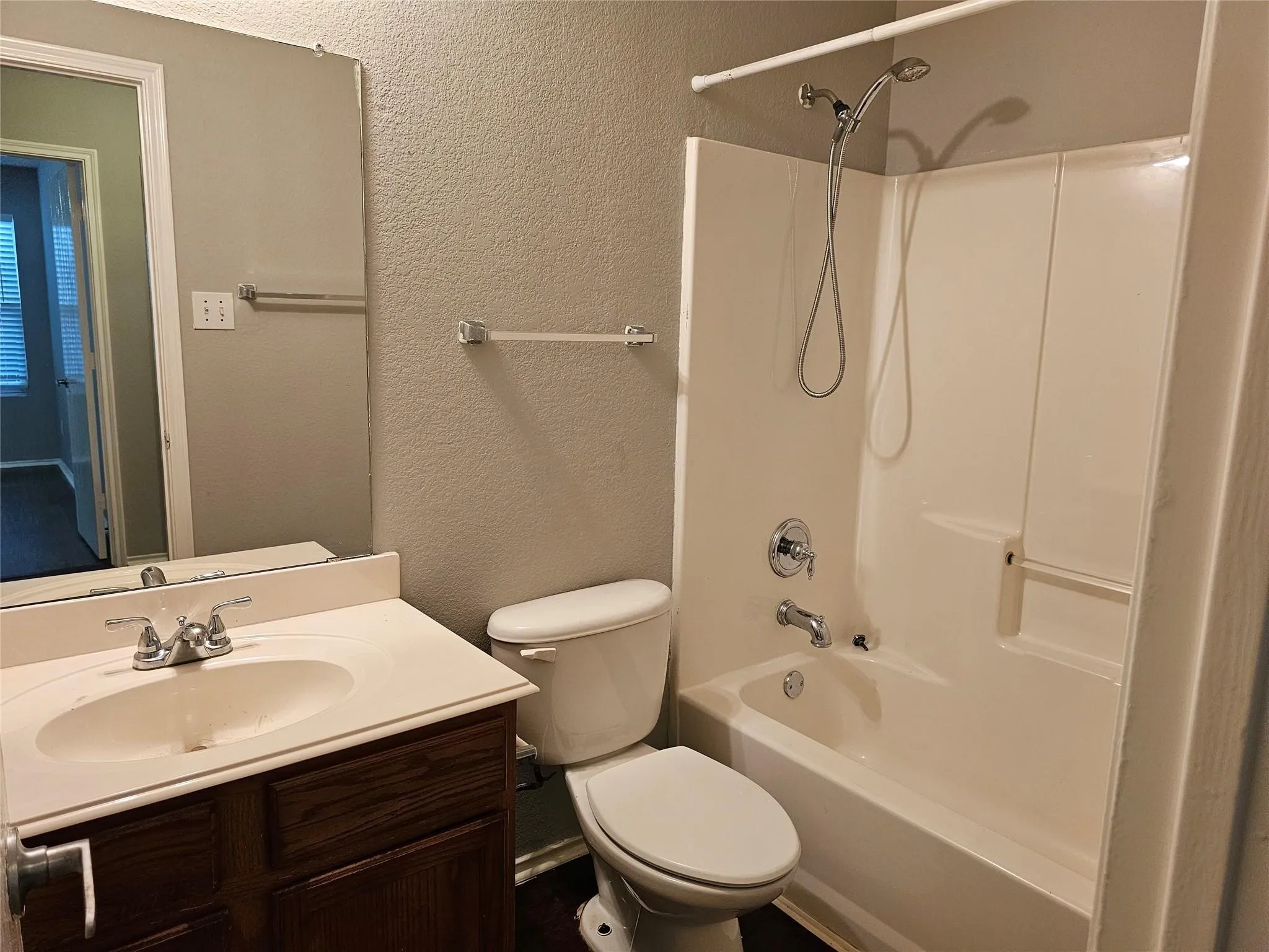 Bathroom with a textured wall, bathtub / shower combination, and vanity