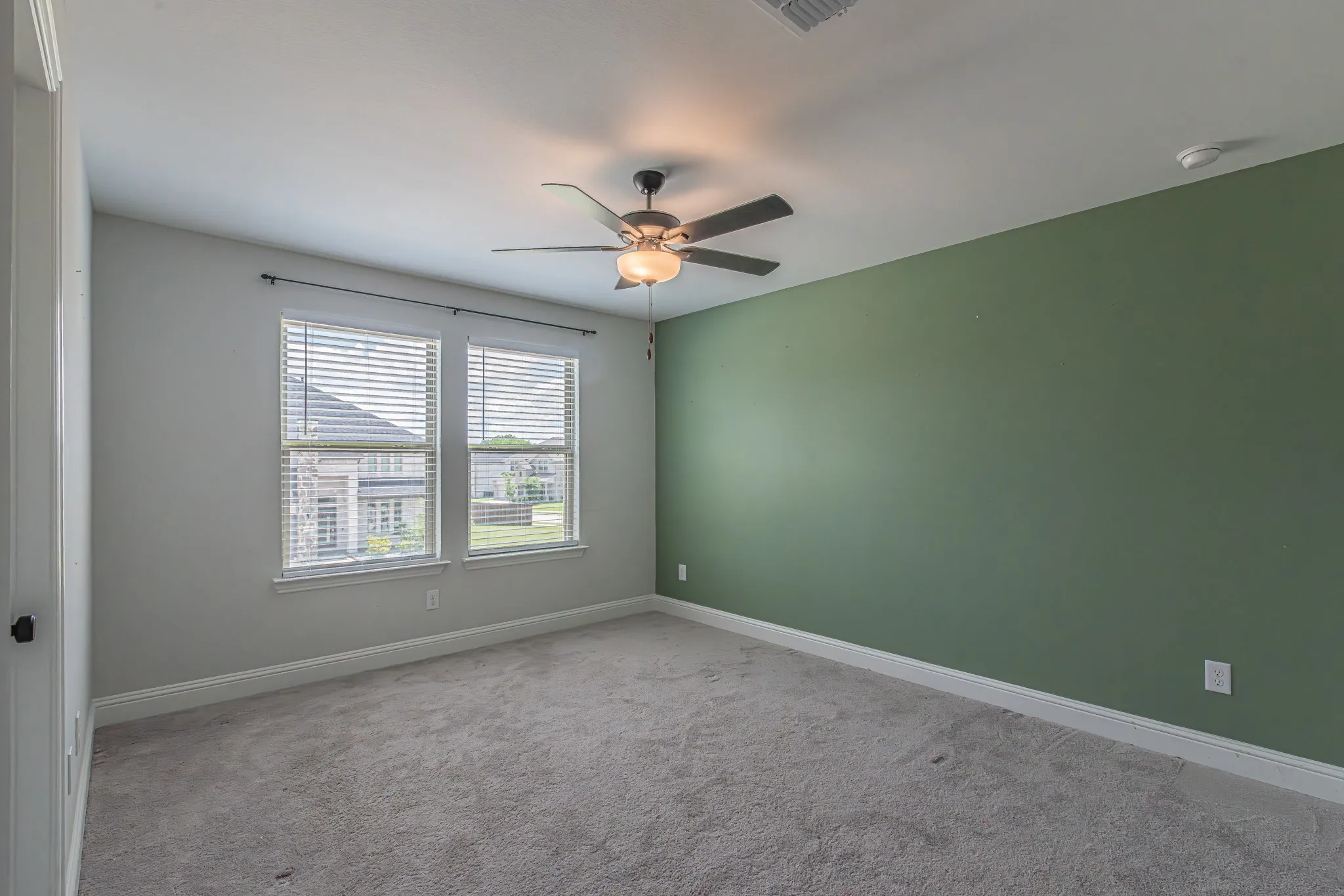 Room featuring a ceiling fan with integrated lighting, a dedicated accent wall, dual windows with blinds, light-toned carpeting, and a white baseboard trim