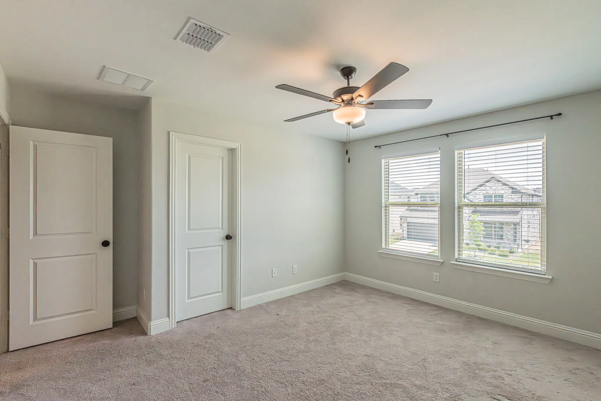 Spacious room featuring neutral carpeting, two panel doors, and a ceiling fan with integrated lighting