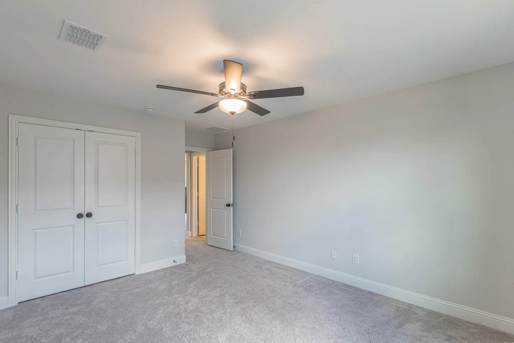 Carpeted interior room featuring a ceiling fan with integrated lighting, bi-fold closet doors with dark hardware, and neutral wall tones