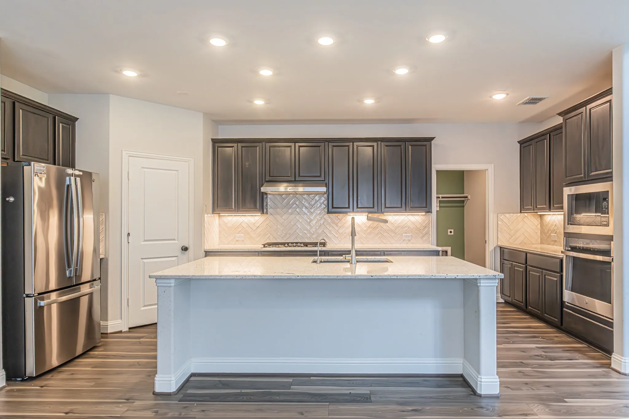 Spacious kitchen featuring an expansive center island, dark wood-finish cabinetry, stainless steel appliances, and wood-finish flooring