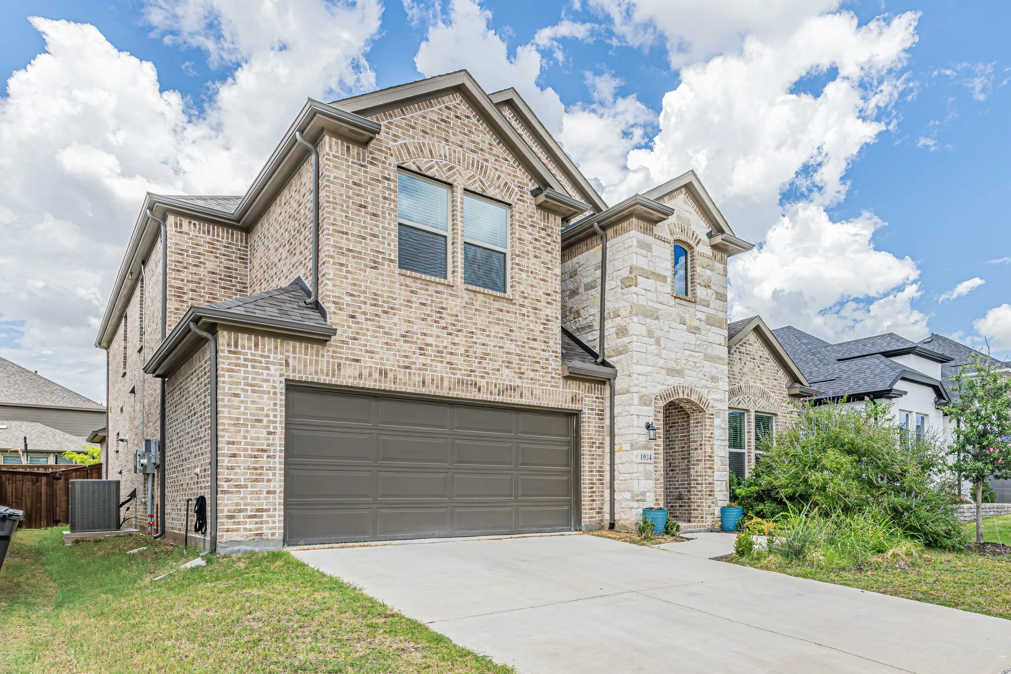 Traditional brick and stone facade featuring a two-car garage, arched entry, and dark shingle roofing