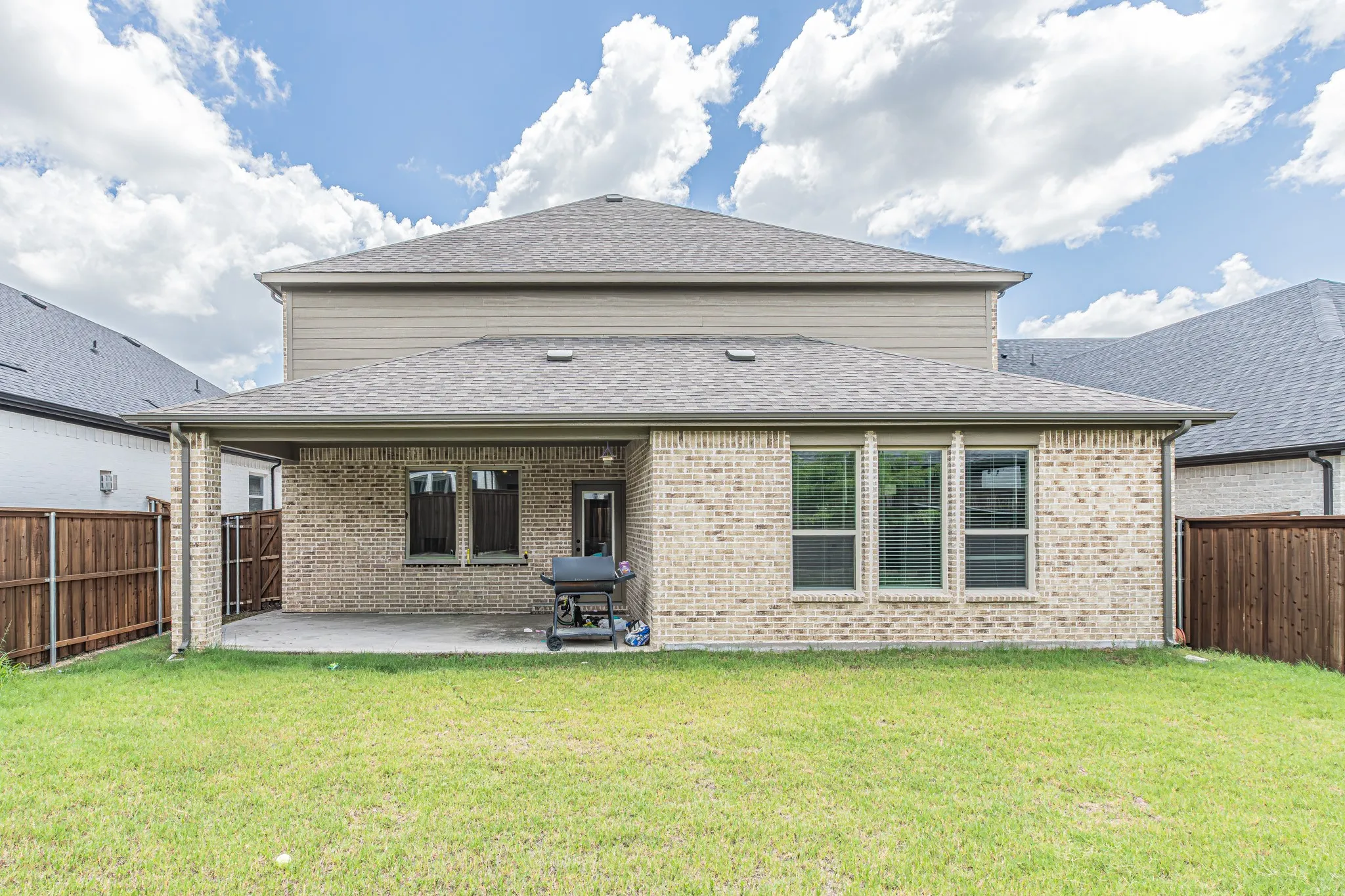 Expansive green lawn with a covered patio featuring a light brick exterior and multiple large windows