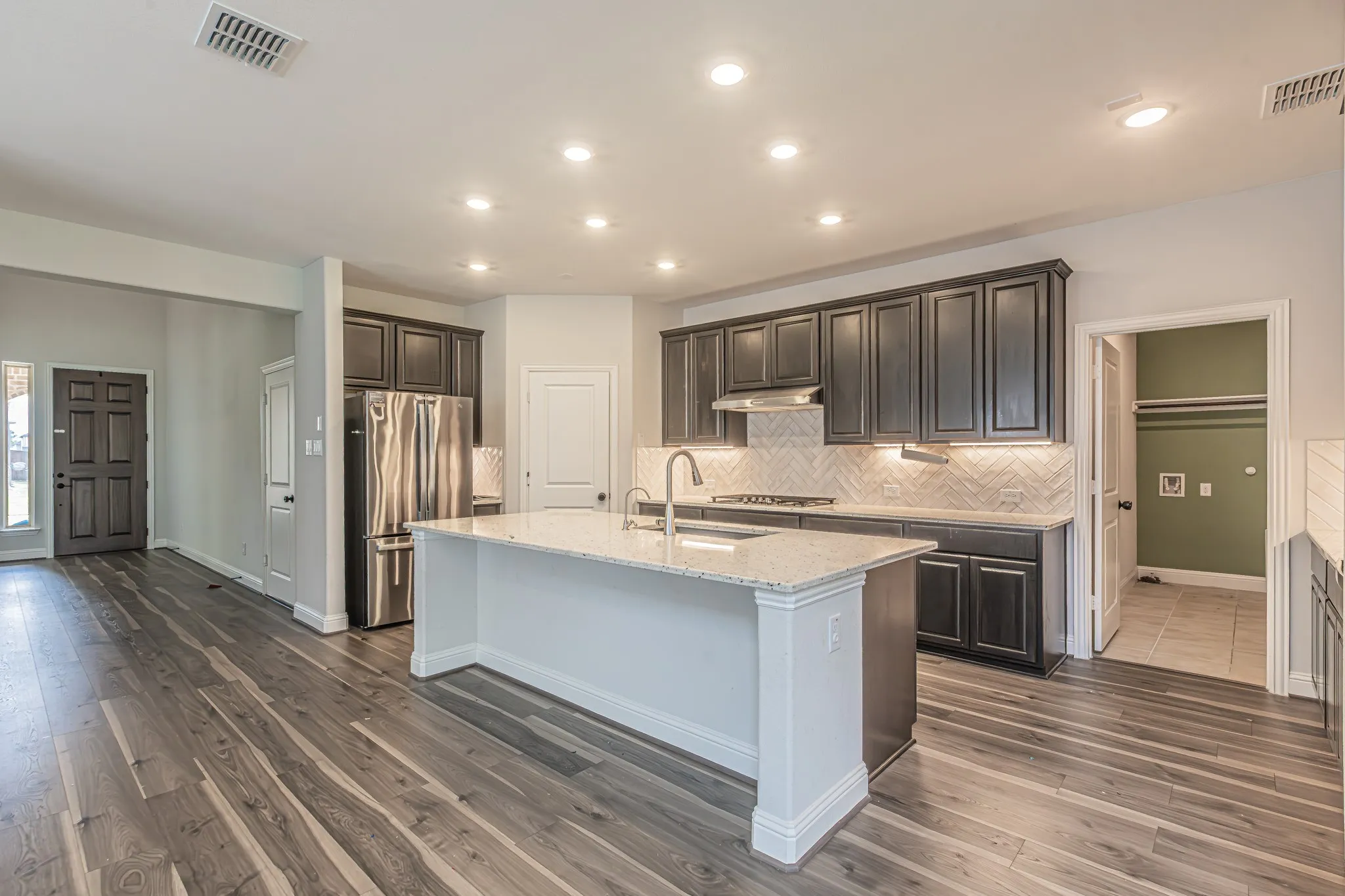 Kitchen featuring dark wood-finish cabinetry, stainless steel appliances, herringbone tile backsplash, and an island with a light-toned countertop