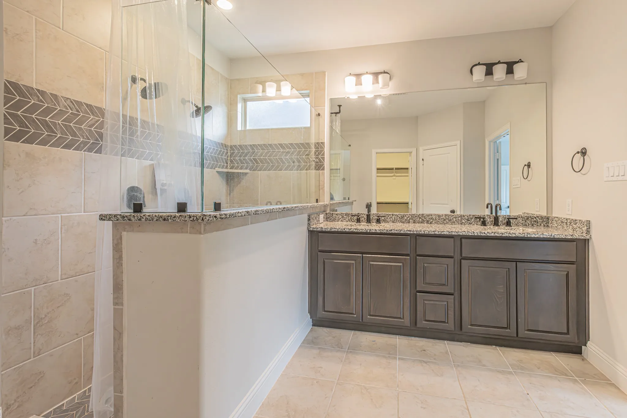 Spacious bathroom featuring a dual vanity with a granite countertop, a large mirror, and a walk-in shower with tile surround and glass enclosure
