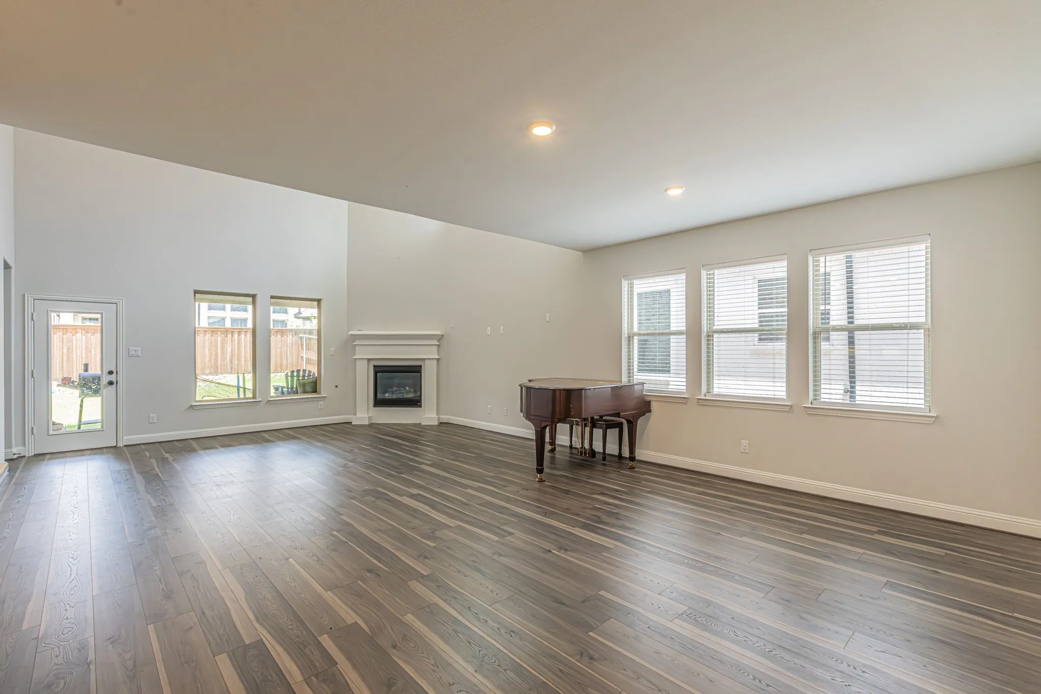 Spacious living area featuring wood-finish flooring, a white mantel fireplace, abundant natural light from multiple windows, and recessed lighting