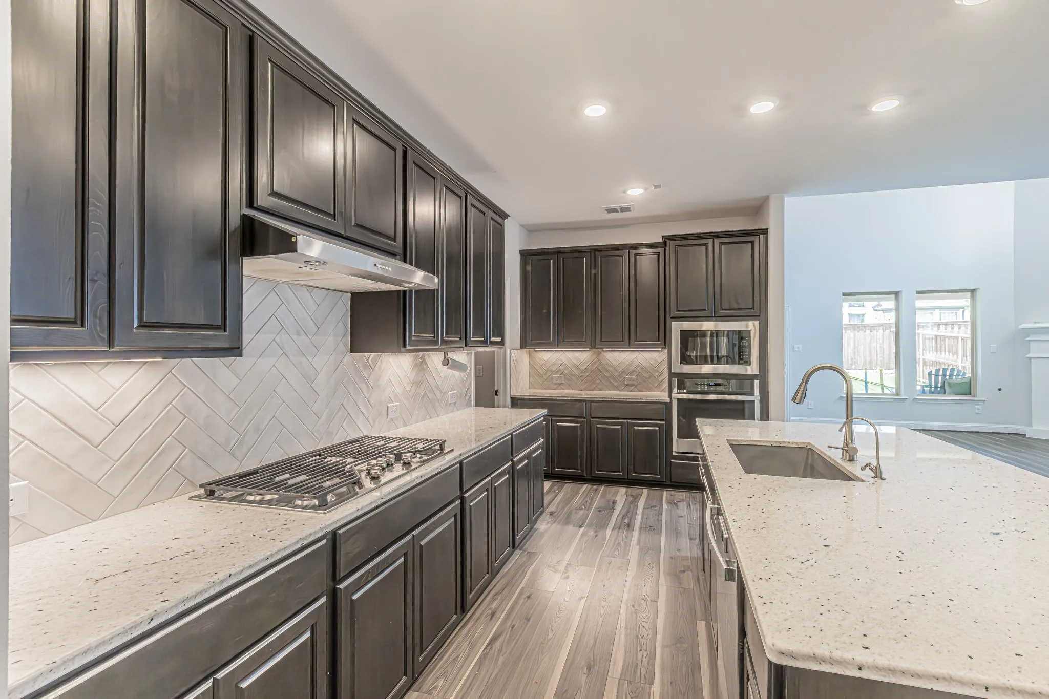 Gourmet kitchen featuring dark wood cabinetry, light-colored speckled countertops, a herringbone tile backsplash, and wood-finish flooring