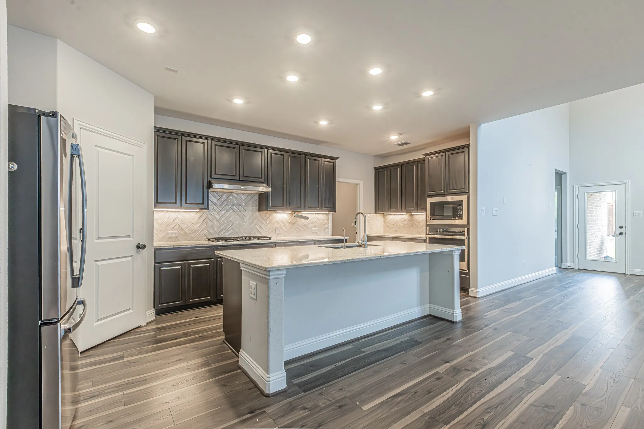Modern kitchen featuring dark wood cabinetry, a light-toned island with integrated sink, and stainless steel appliances