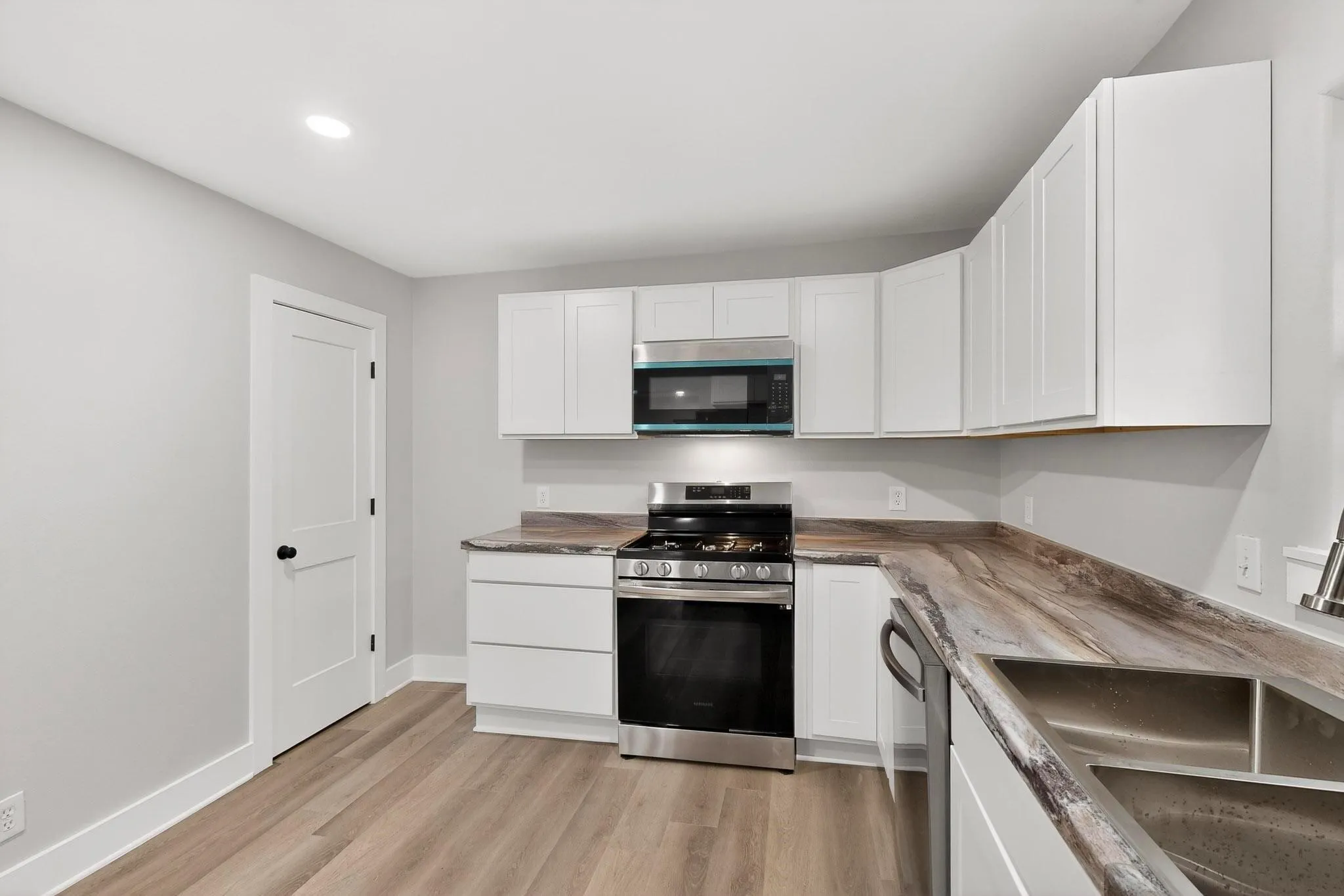 Modern kitchen featuring white shaker-style cabinetry, wood-finish flooring, and a stainless steel oven/range with an overhead microwave