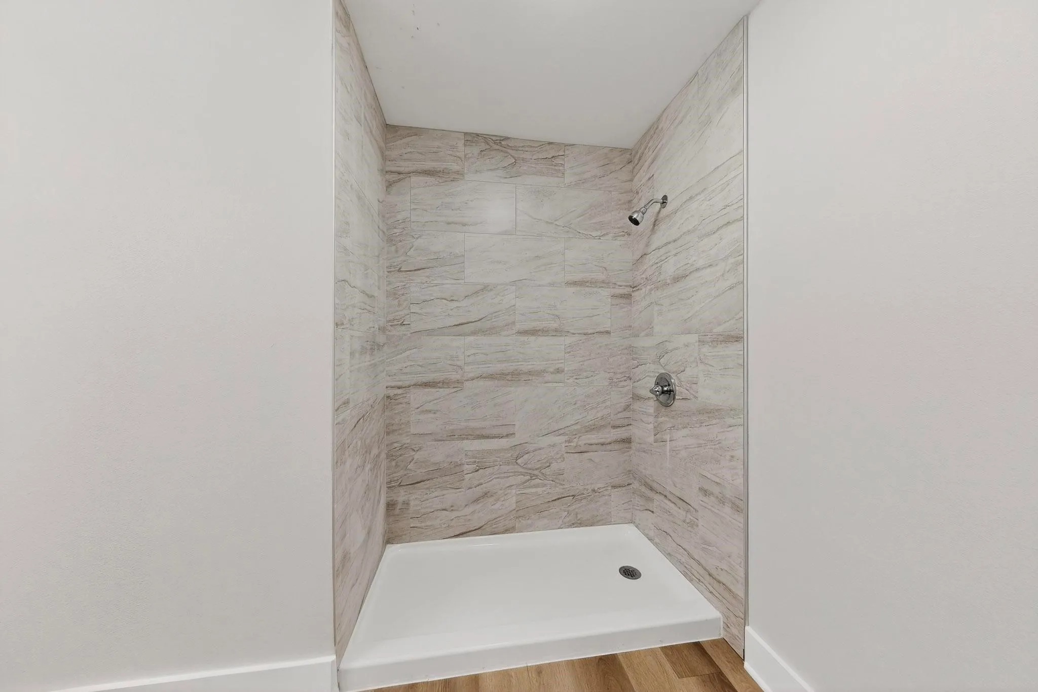 Walk-in shower featuring light-toned, horizontally laid tile walls with natural veining and a white shower pan